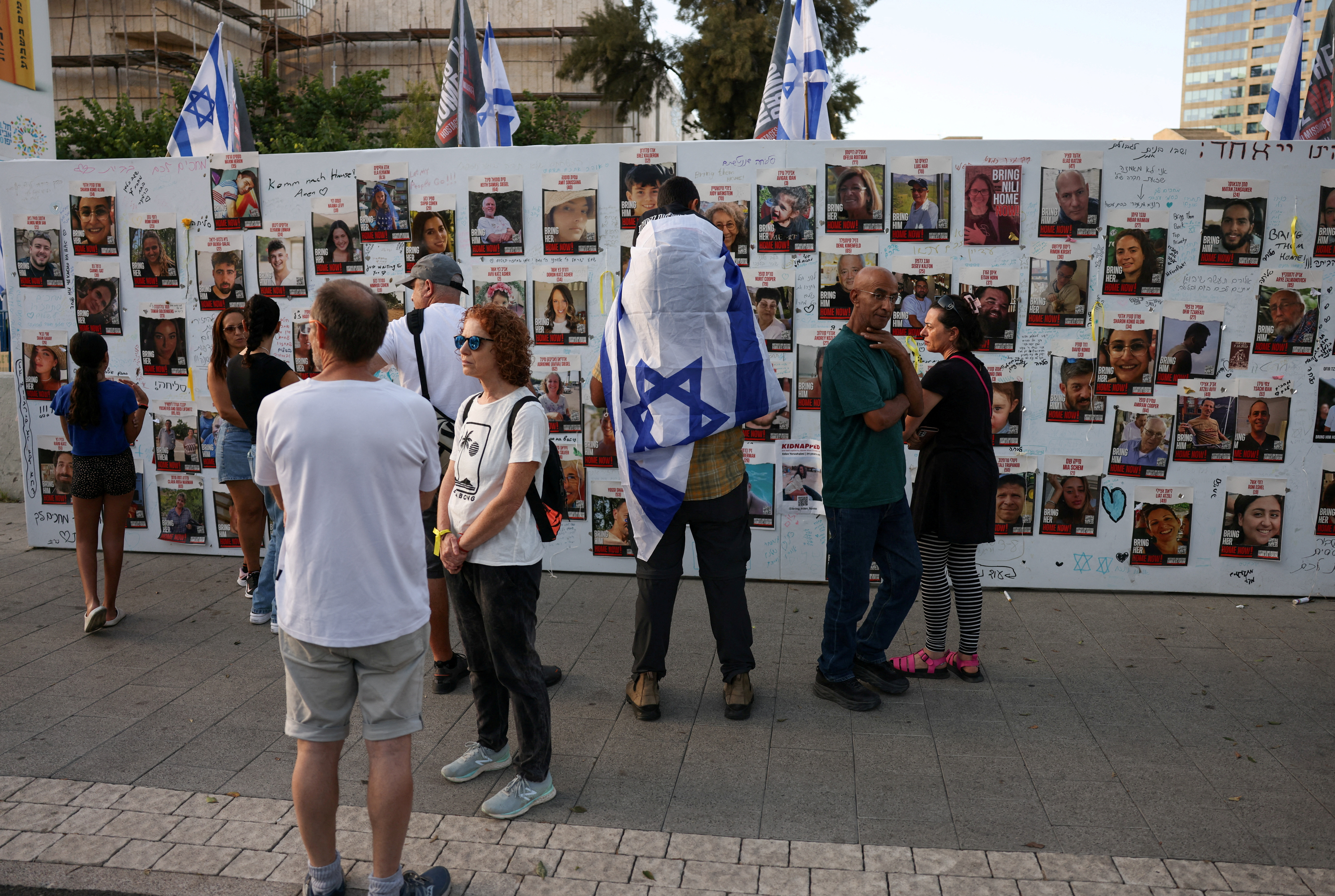 People stand next to the wall with pictures, dedicated to hostages that are being held in Gaza after they were kidnapped from Israel by Hamas gunmen on October 7, as families and supporters of hostages hold a demonstration calling for their immediate release in Tel Aviv, Israel November 3, 2023. 