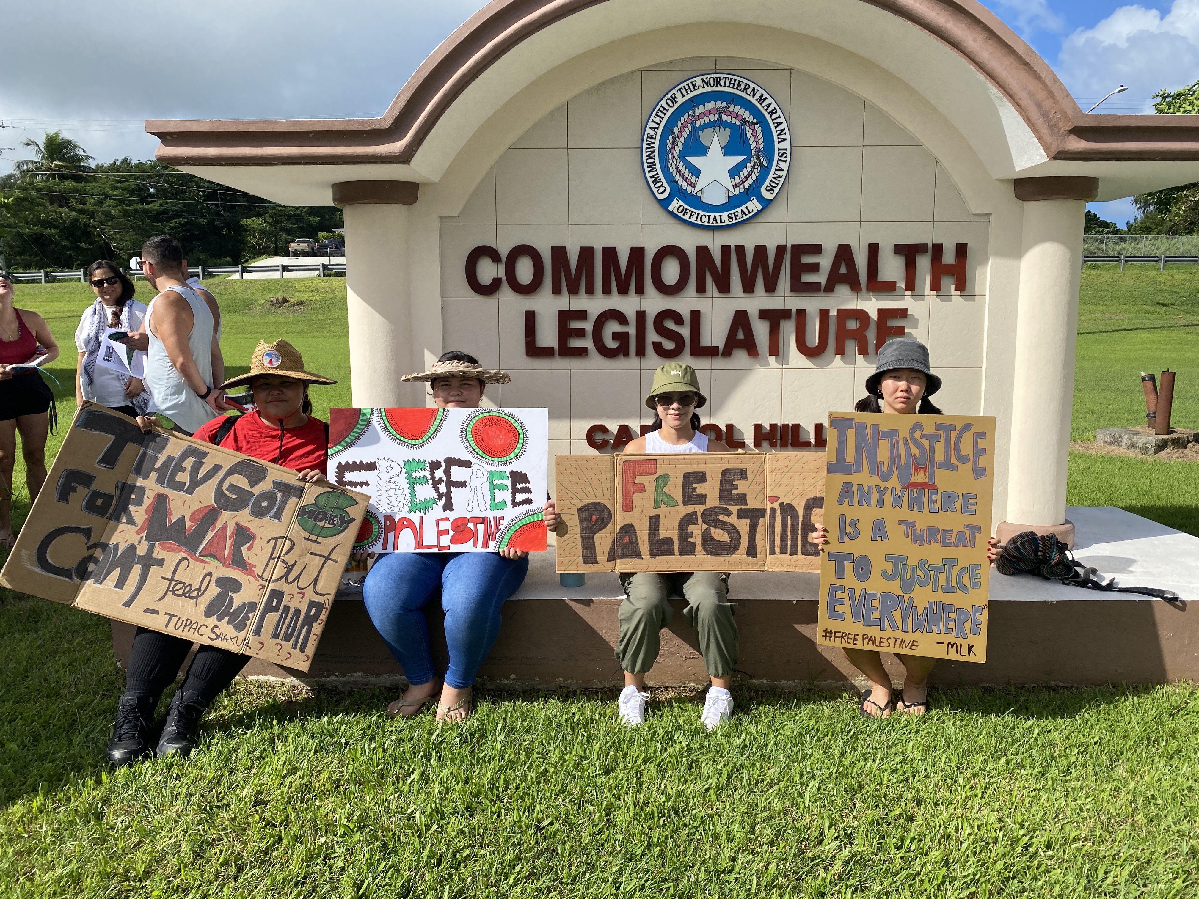 Protestors hold signs outside the CNMI legislative building.