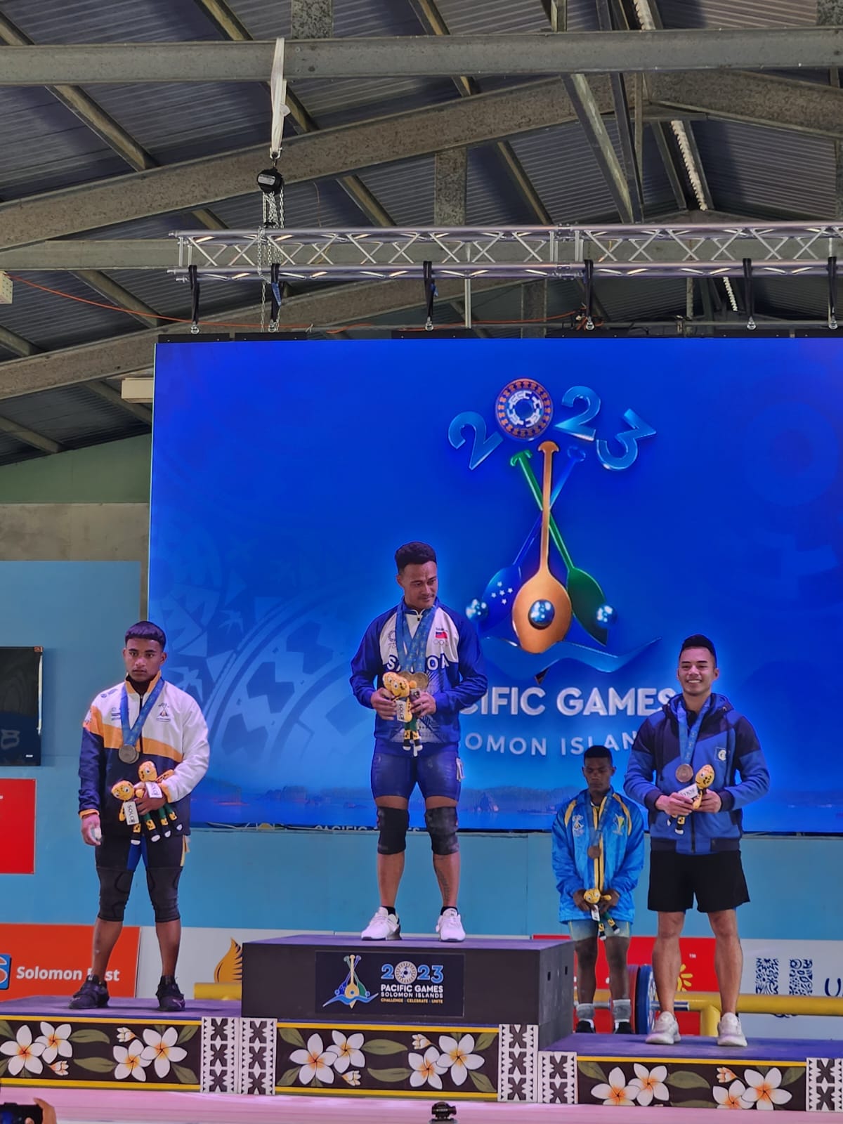 The NMI's Leowell Cristobal, right, makes it to the podium after placing third in the clean & jerk event in the men's 67kg class of the weightlifting competition in the 2023 Pacific Games at the Maranatha Hall in Honiara, the Solomon Islands.