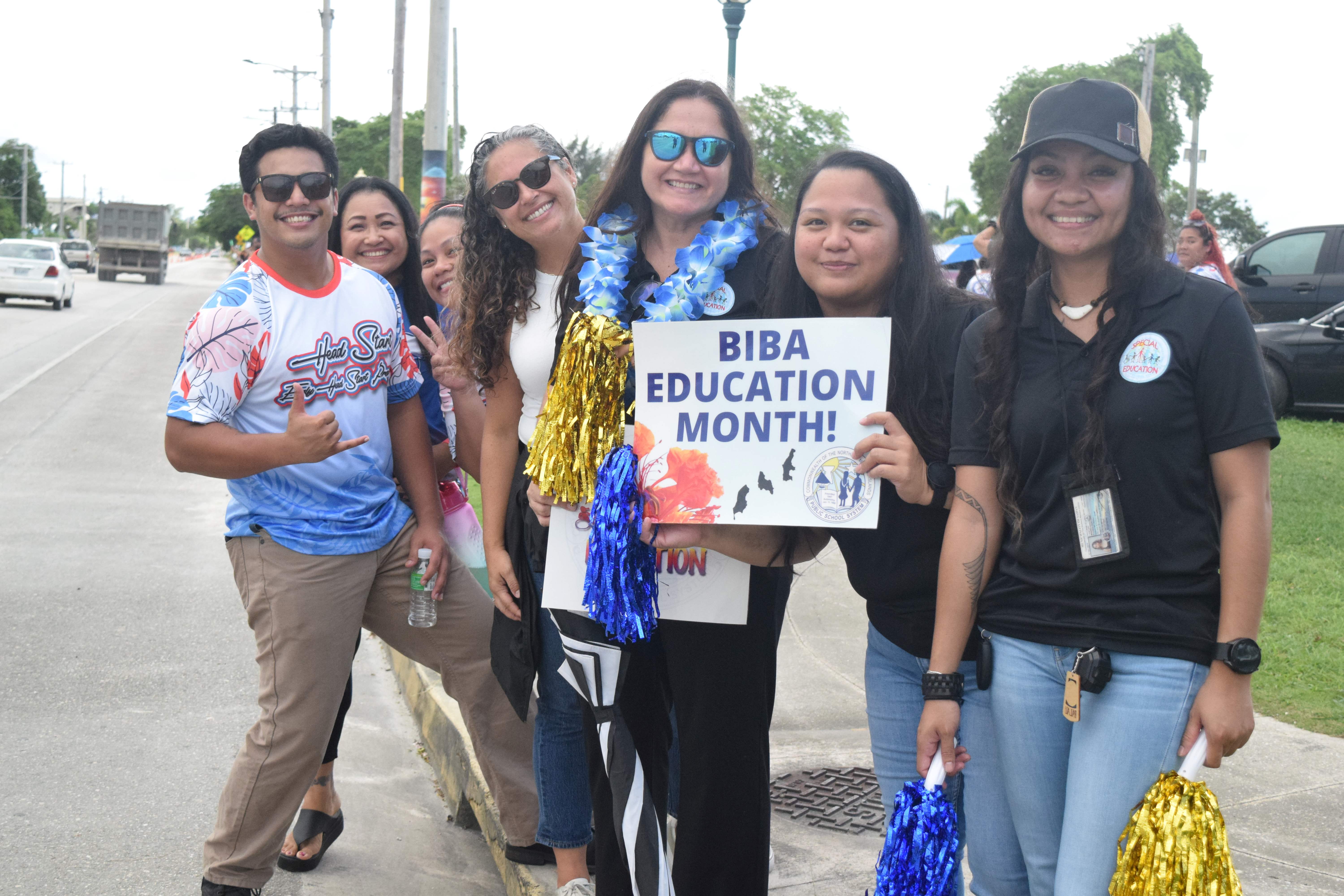 Interim Education Commissioner Donna Flores, center, and Public School System staff participate in a roadside waving activity at Garapan Fishing Base on Monday.