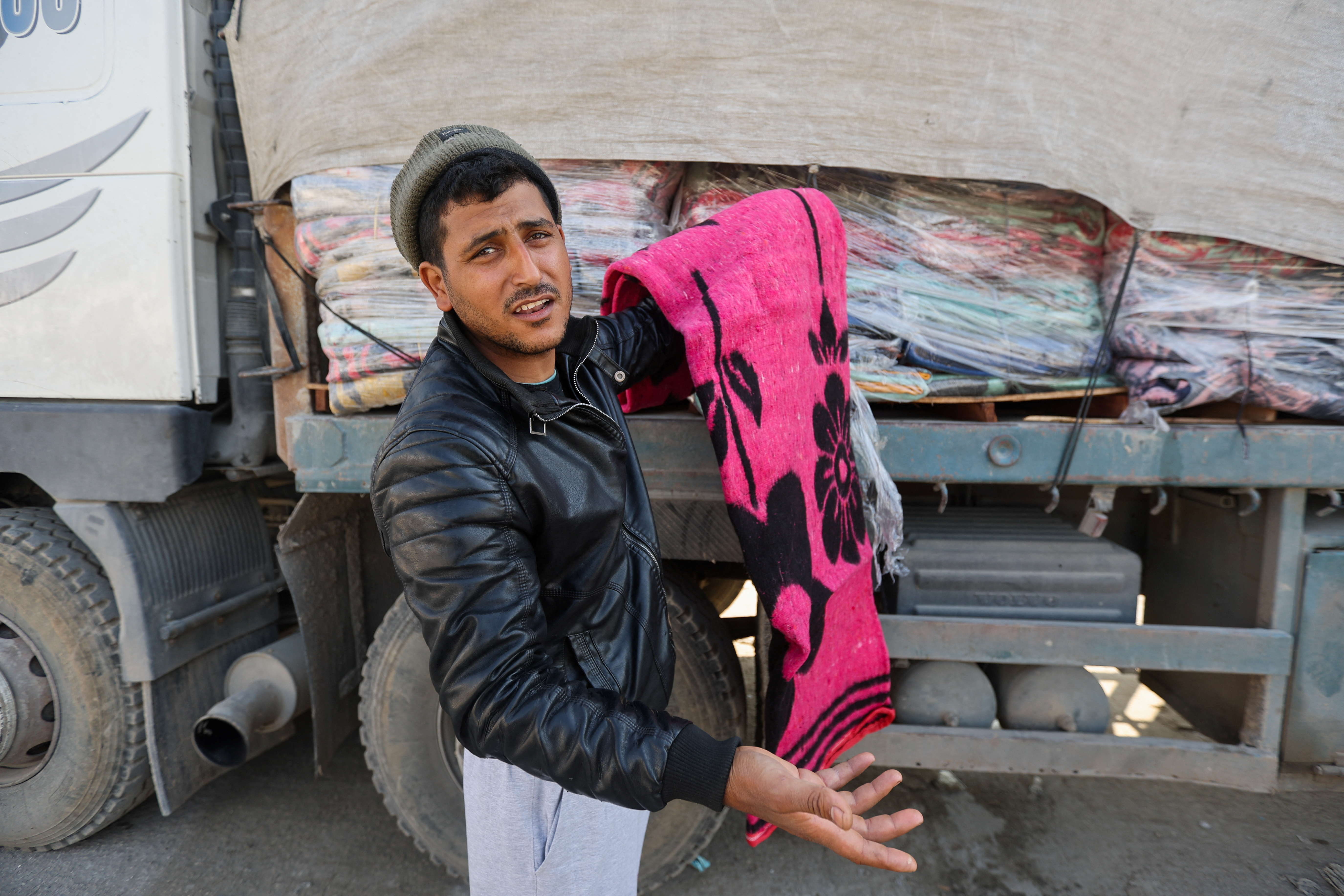 A man holds a blanket beside a truck carrying aid at the Rafah border, amid the ongoing conflict between Israel and the Palestinian Islamist group Hamas, in Rafah in the southern Gaza Strip, December 18, 2023. 
