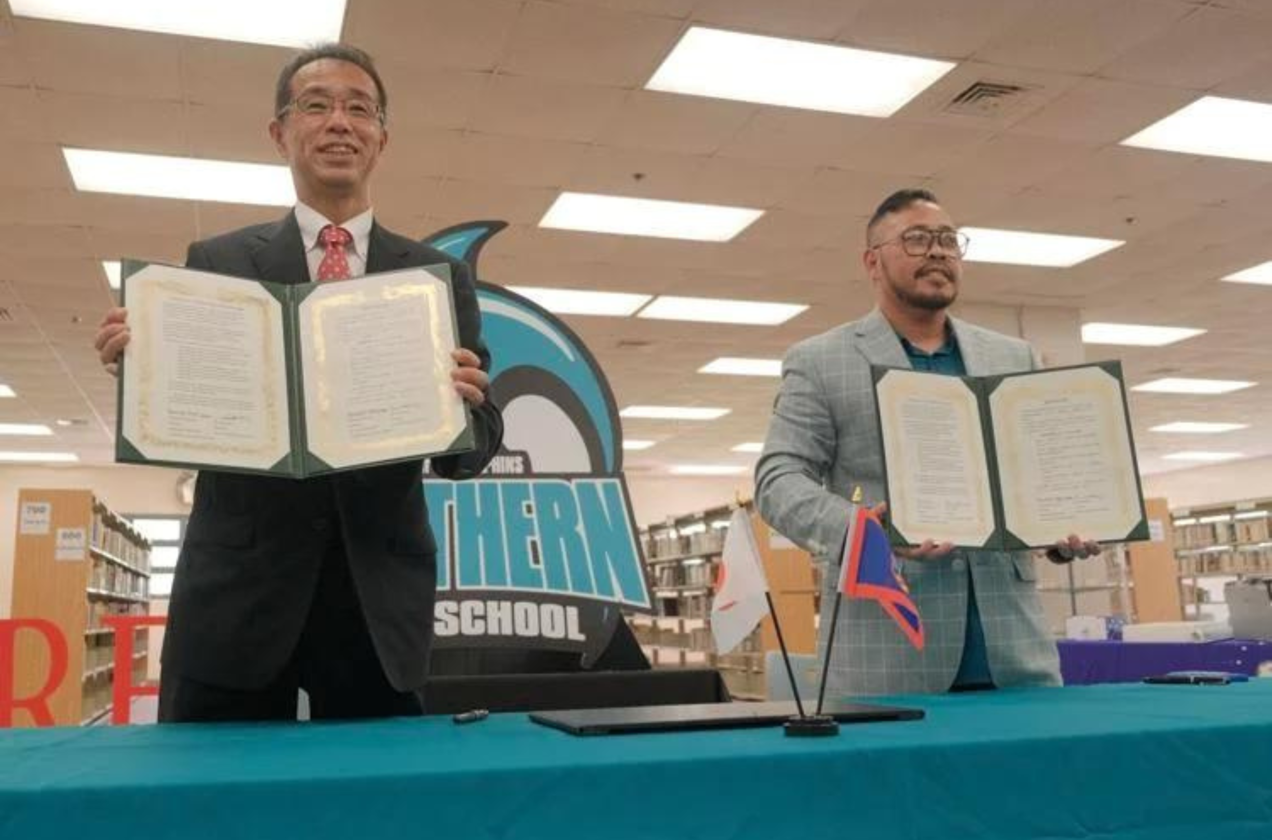 Yasuyuki Moriyama, principal of Okayama Higashi Commercial High School, left, and Southern High School Principal Michael Meno display certificates after a sister school partnership signing ceremony at Southern High School in Sånta Rita-Sumai on Thursday, Dec. 14, 2023. 