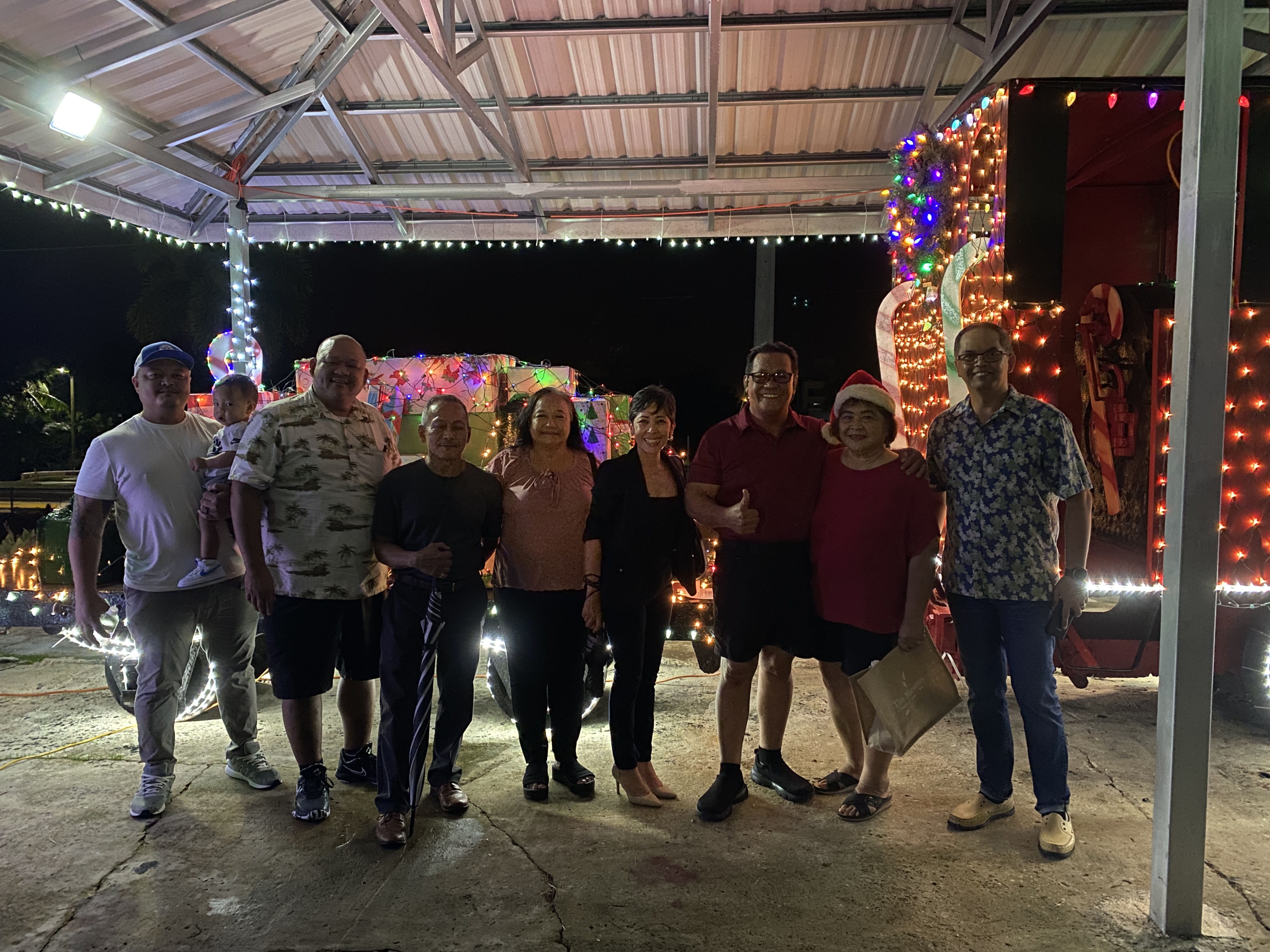From left, Rep. Angelo Camacho, Rep. John Paul Sablan, Rep. Vicente Camacho, Saipan and Northern Islands Municipal Council Member Carmen Pangelinan, Rep. Marissa Flores, Saipan Mayor RB Camacho, his wife, and Pastor Eric Abragan, pose for a picture near the brightly decorated train engine.
