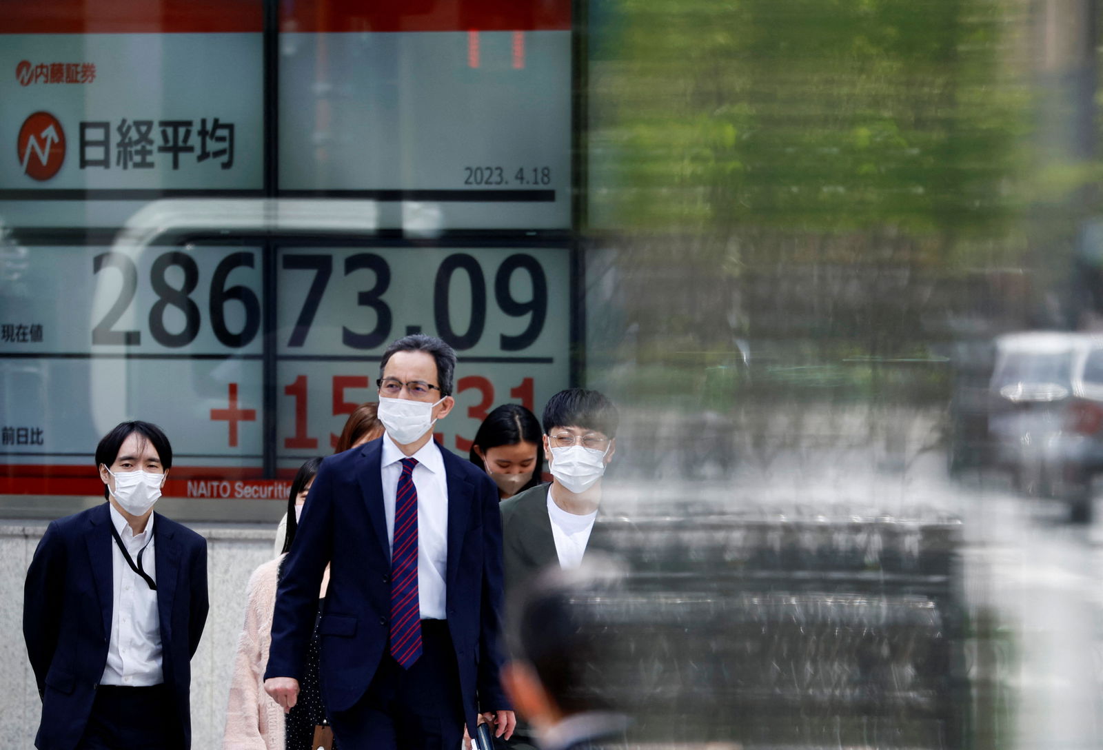 Passersby walk past an electric board displaying Japan's Nikkei share average outside a brokerage in Tokyo, Japan, April 18, 2023.
