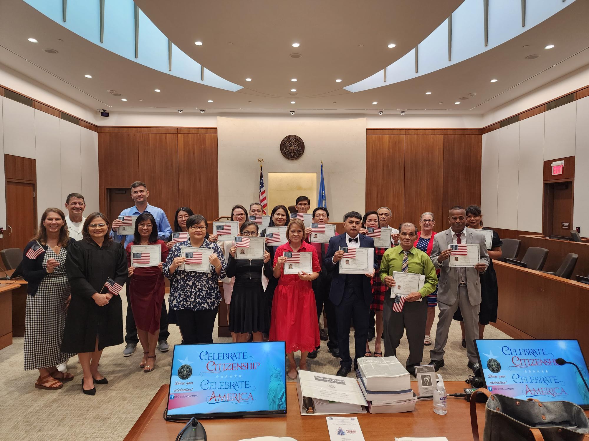 The commander of Joint Region Marianas, Rear Adm. Gregory C. Huffman, and wife Judy Huffman pose for a photo with Chief Judge Ramona V. Manglona of the District Court for the NMI, U.S. Citizenship and Immigration Services Officer Patricia Phelan, and the 17 new American citizens at the federal courthouse on Monday, Dec. 11, 2023.