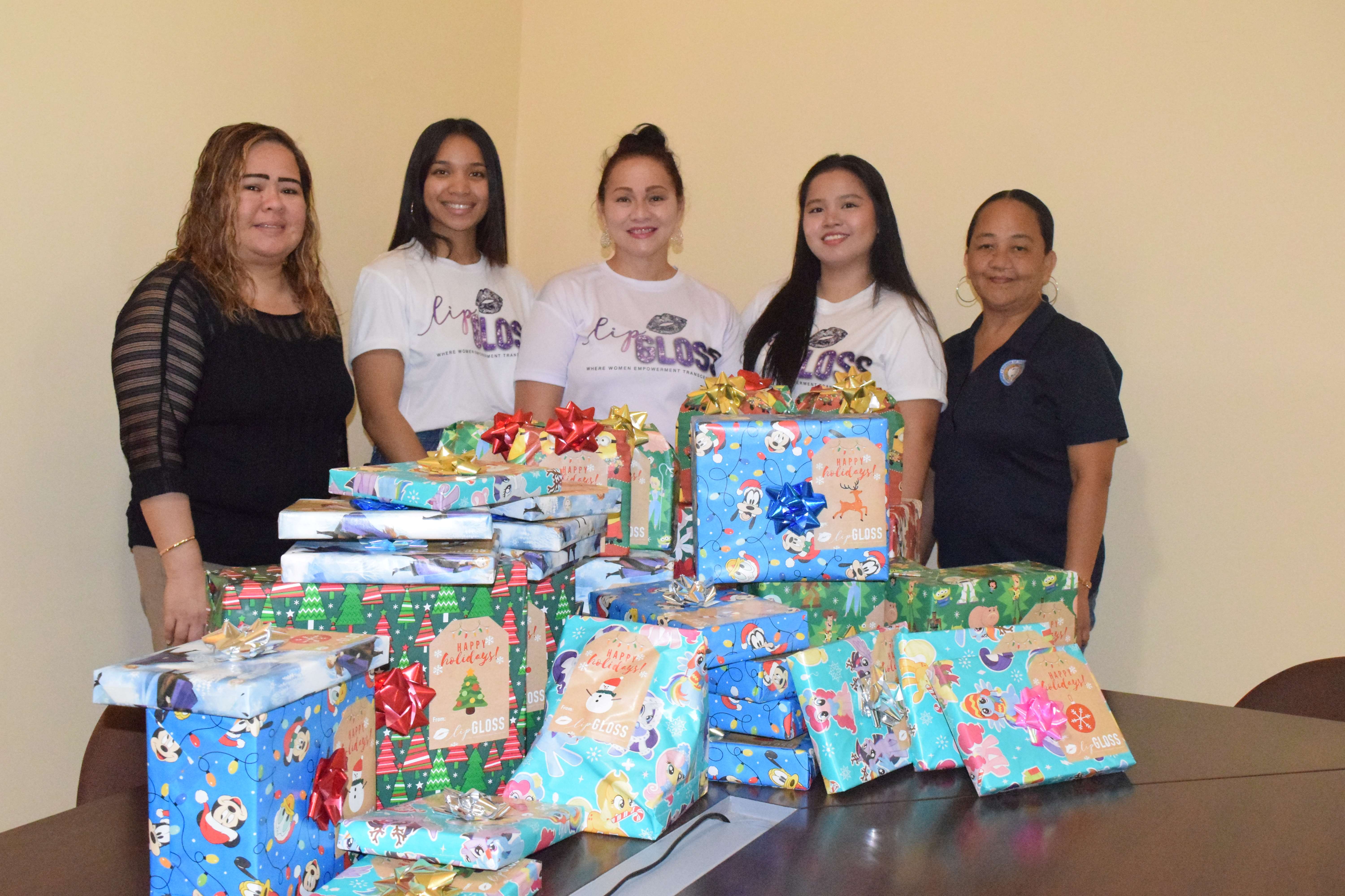 Lip Gloss Founder and Chief Executive Officer Maryann Borja, center, acting Department of Community and Cultural Affairs Secretary Vivian Sablan, left, Lip Gloss President Darsha Camacho, second left, Treasurer Hazel Sadian, second right and DYS Shelter Supervisor Junnie S. Masga pose for a photo next to the gifts for children under the care of the Division of Youth Services at the DYS office on Capital Hill, Thursday.