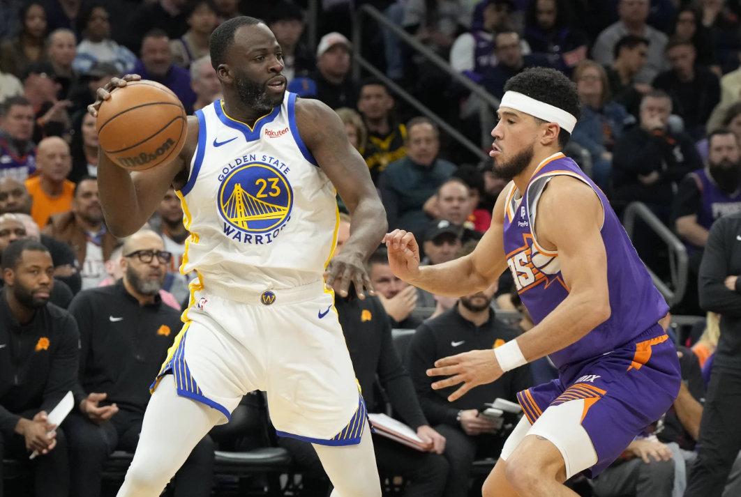 Golden State Warriors forward Draymond Green shields the ball from Phoenix Suns guard Devin Brooker during the first half of an NBA game, Tuesday, Dec. 12, 2023 in Phoenix.