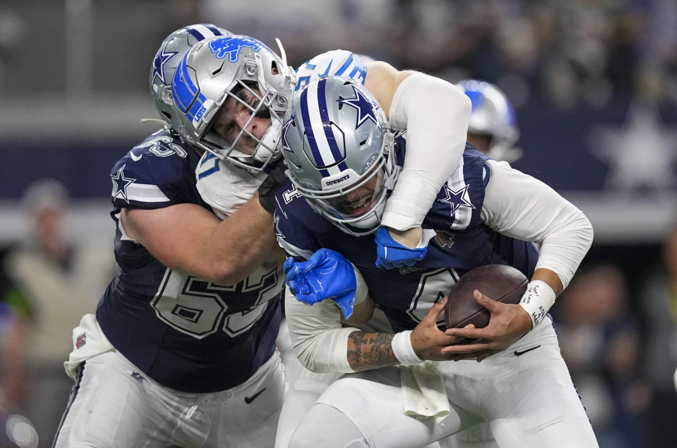 Dallas Cowboys quarterback Dak Prescott, right, is sacked by Detroit Lions defensive end Aidan Hutchinson, center, as Cowboys center Tyler Biadasz (63) tries to block during the first half of an NFL game, Saturday, Dec. 30, 2023 in Arlington, Texas.