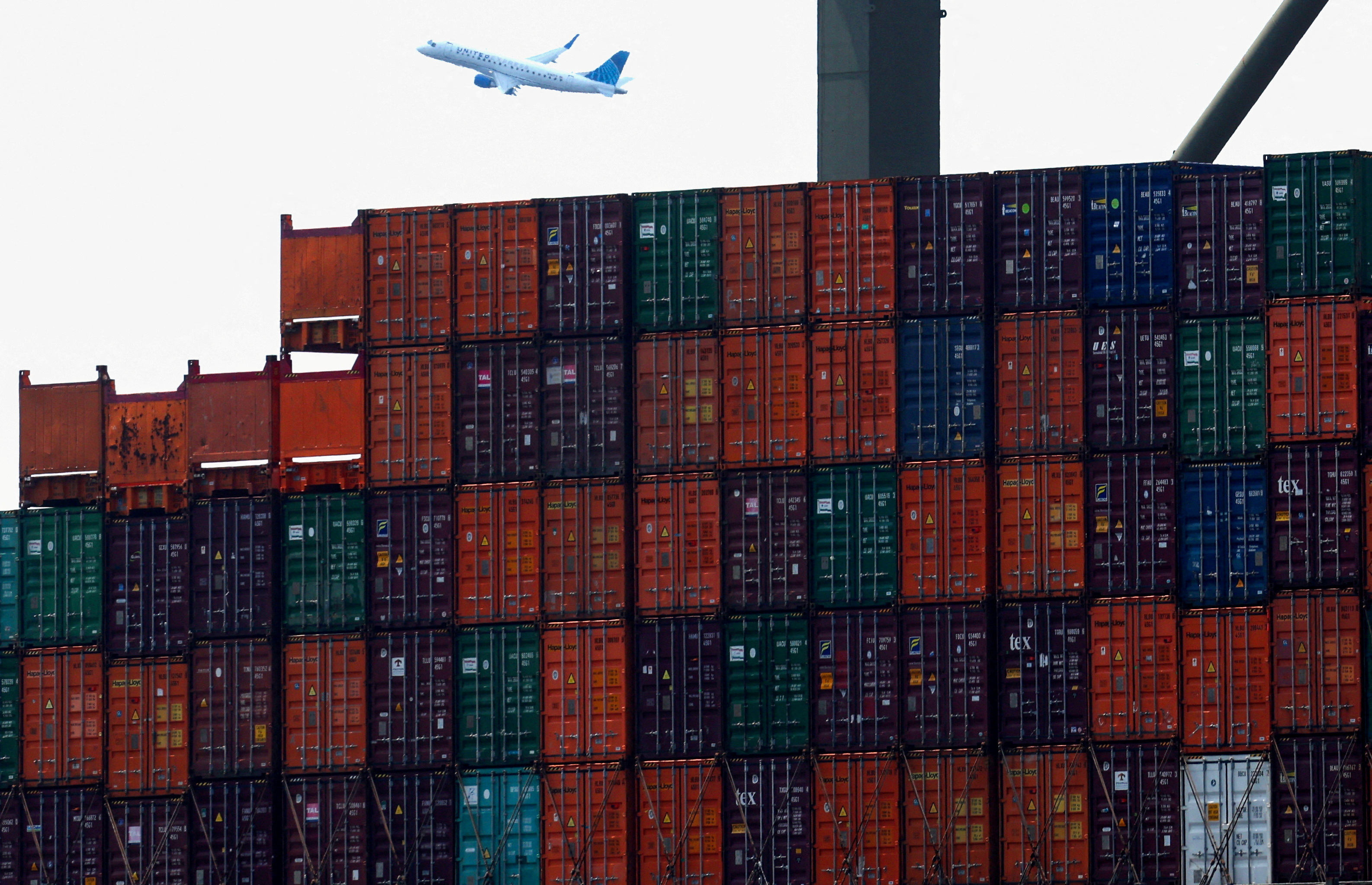 Shipping containers are seen stacked on a docked cargo ship as a passenger airplane takes off from Newark Airport, in Port Elizabeth, New Jersey, U.S., July 12, 2023. 