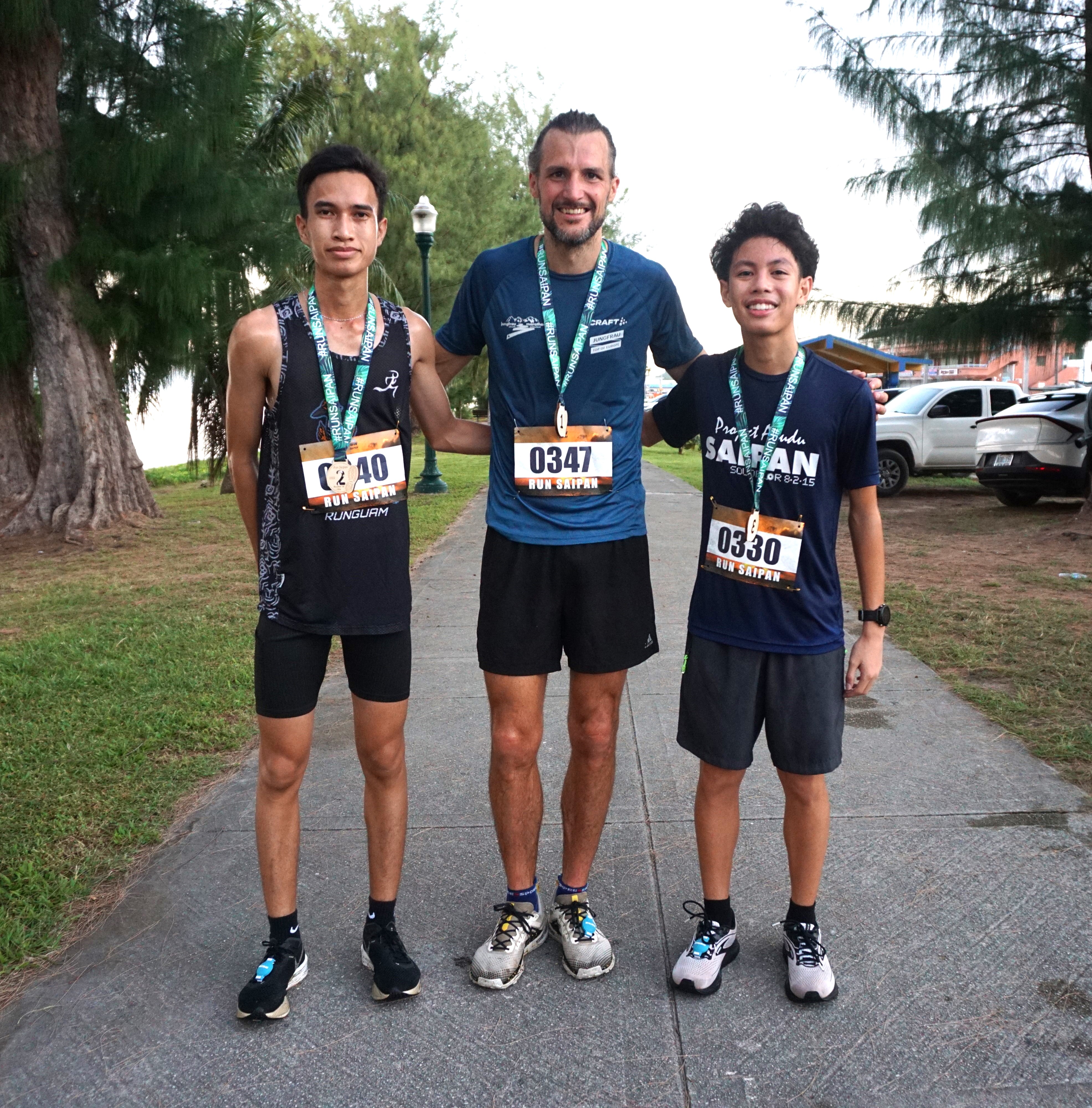 Martin Hess, center, Sildrey Veloria, left, and Victor Nash Santos pose for a photo as the top three finishers of the 10K distance race on day 1 of the 2nd Annual Run Saipan Trinity at the Beach Road pathway on Saturday.
