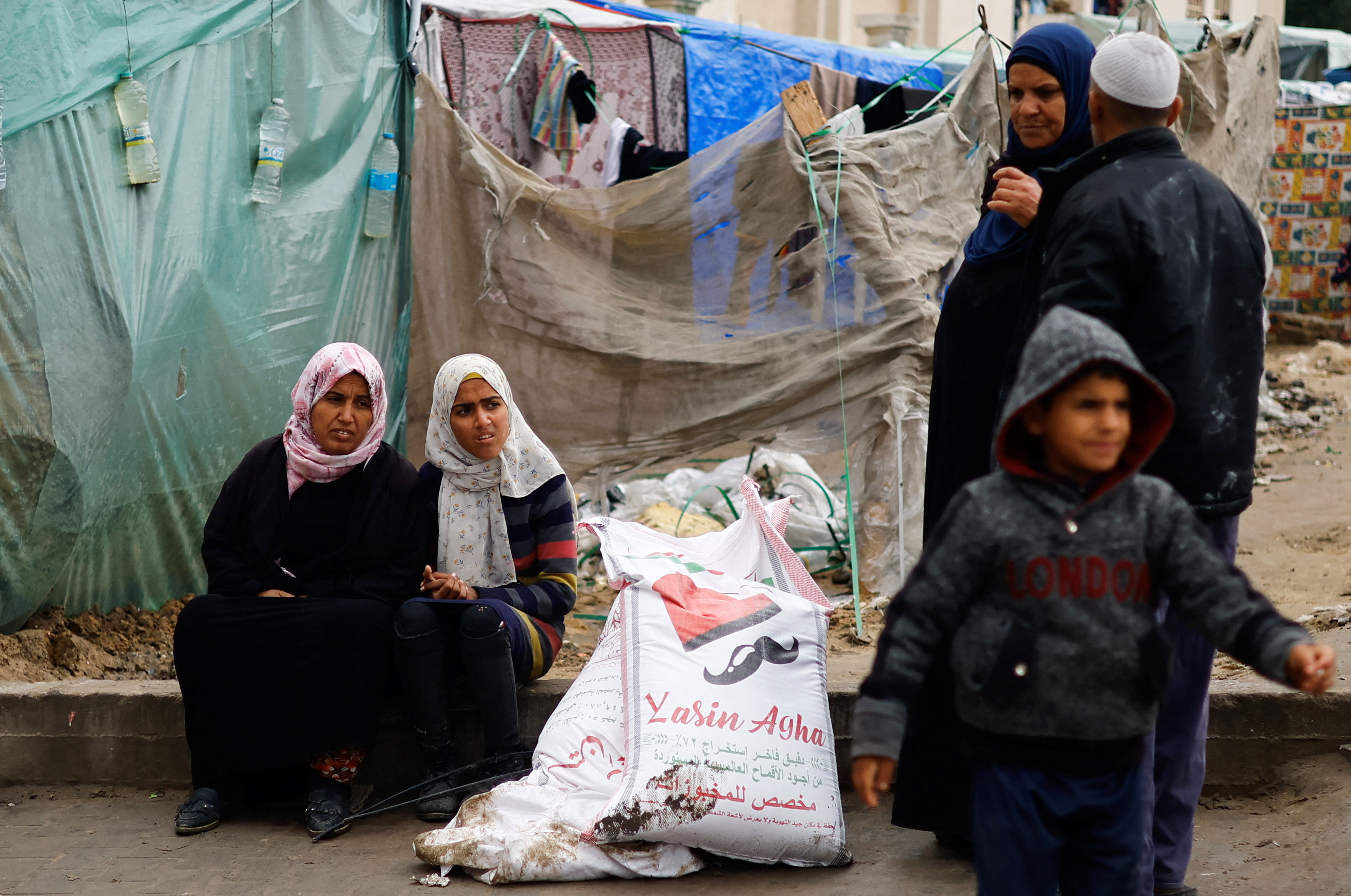Palestinian women sit near bags of flour distributed by the United Nations Relief and Works Agency (UNRWA), amid the ongoing conflict between Israel and Hamas, in Rafah in the southern Gaza Strip January 29, 2024. 
