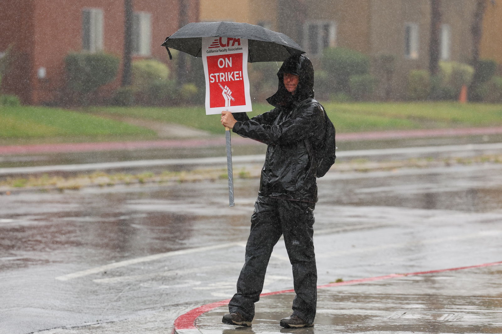 A person holds an umbrella and a sign while picketing begins at San Diego State University, as the California Faculty Association, the union representing 29,000 professors, lecturers, librarians, counselors and coaches across the California State University, start a planned five-day strike in San Diego, California, U.S. January 22, 2024. 