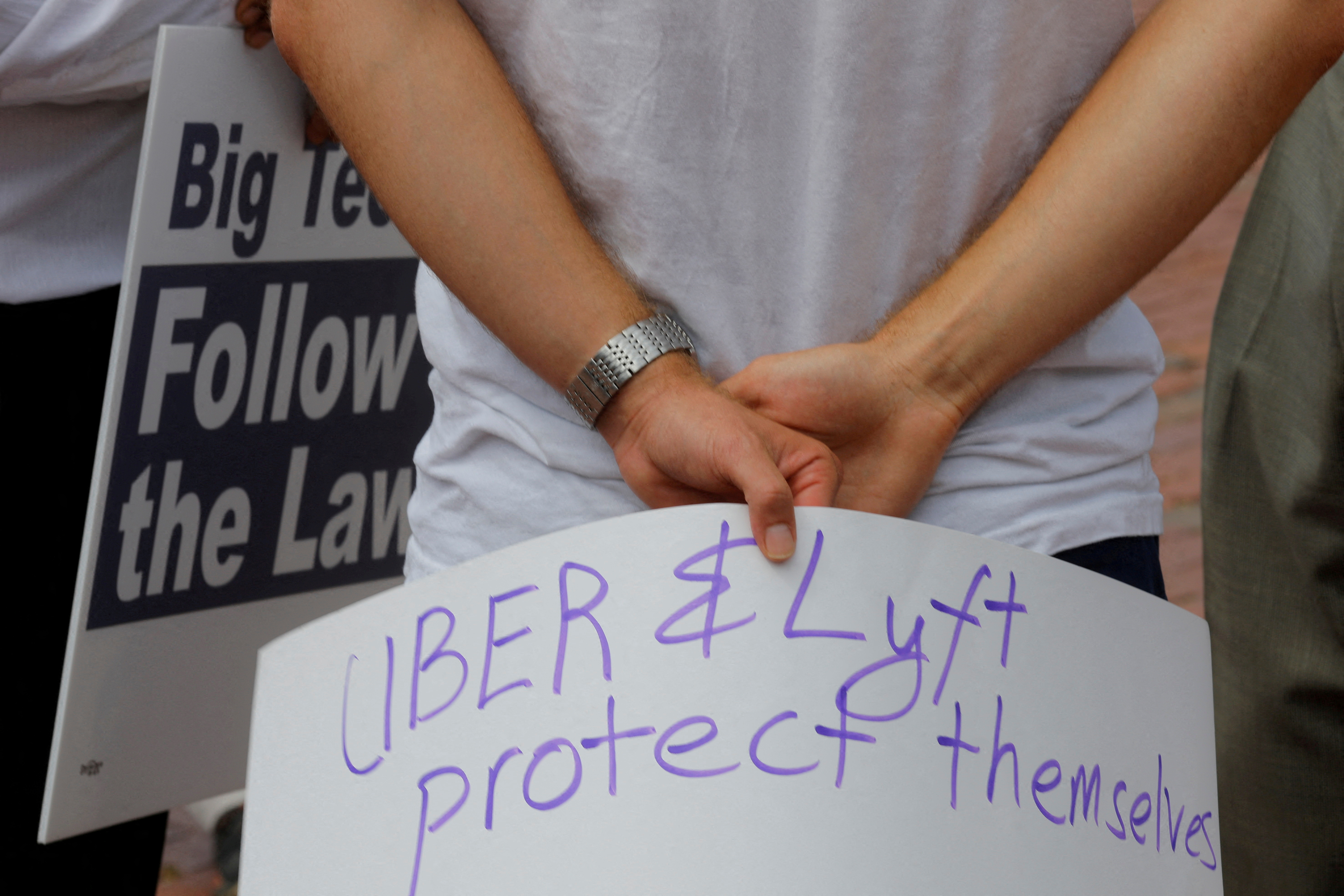 A man holds a sign reading “Uber and Lyft Protect Themselves” at a demonstration opposing a ballot campaign by companies such as Uber, Lyft and Door Dash to exempt their companies from some labor laws, outside the Massachusetts Statehouse in Boston, Massachusetts, U.S., June 22, 2021. 
