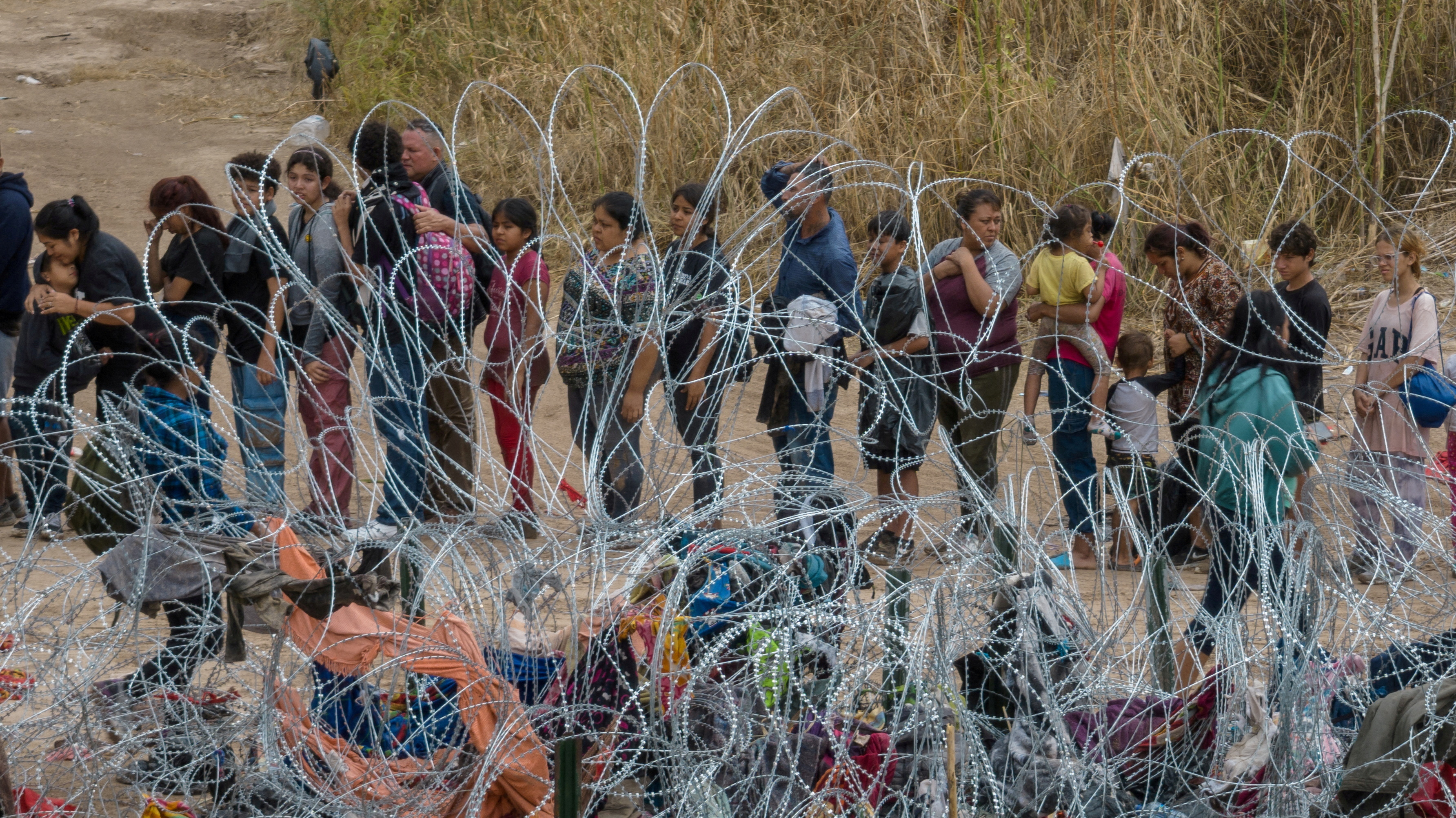 Migrants, most from Venezuela, stand near razor wire while surrendering to authorities after wading across the Rio Grande river into the United States from Mexico, in Eagle Pass, Texas, U.S. October 5, 2023. 