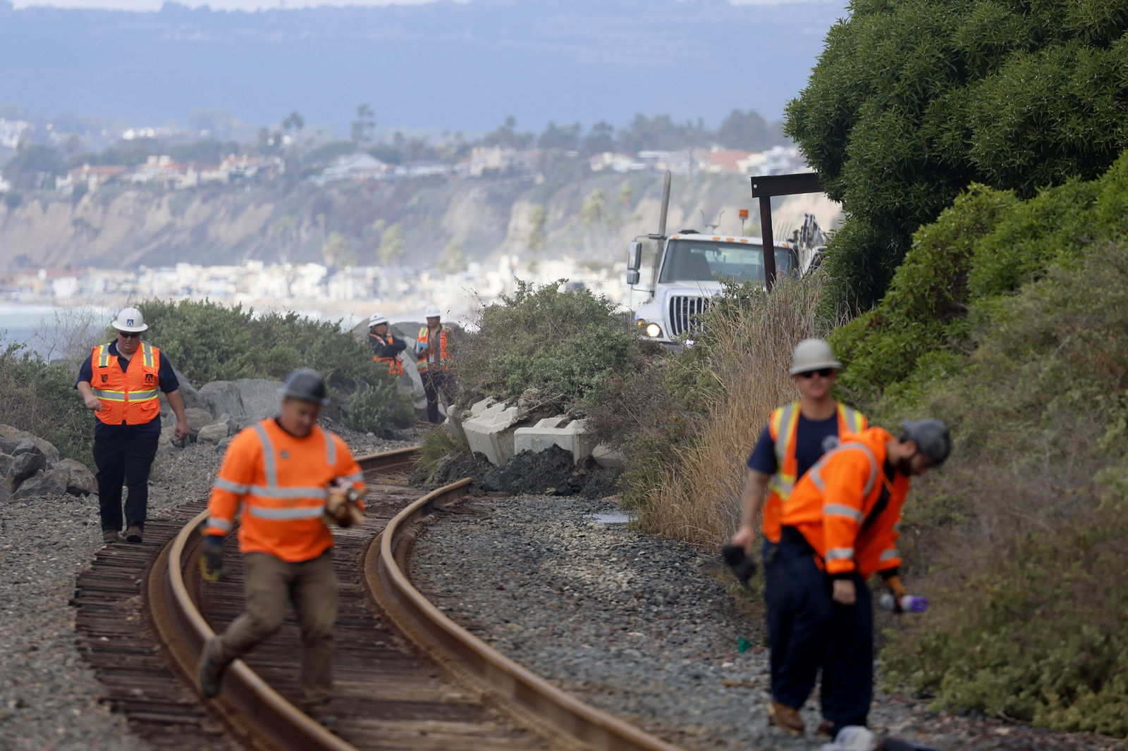 On Jan. 25, 2024, workers in San Clemente, California, continue to clear railroad tracks following a landslide a day prior that sent boulders and debris onto the tracks and damaged the Mariposa Trail Bridge. 