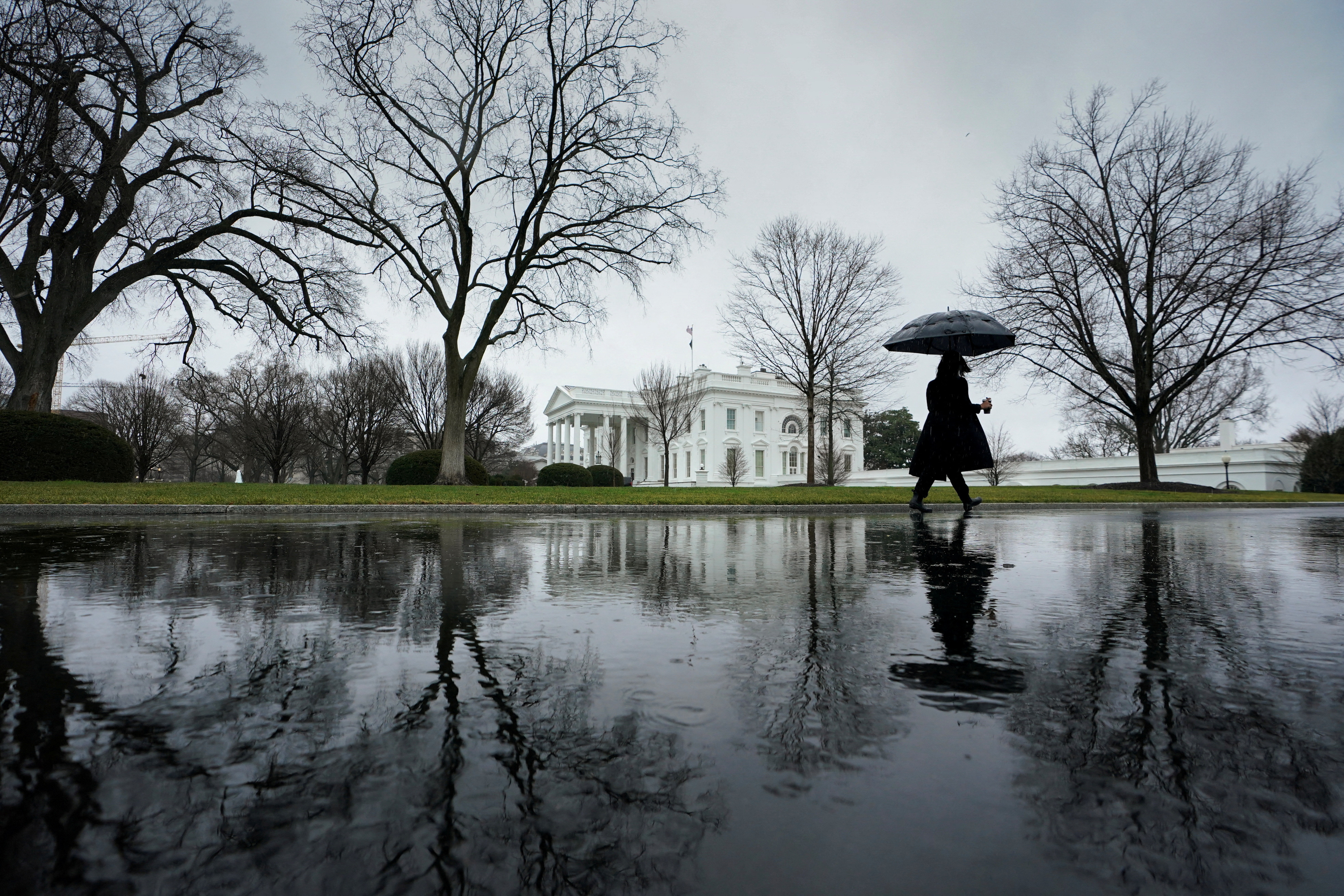 A reporter, arriving for work, walks up the driveway toward the White House on a rain-soaked morning in Washington, U.S., January 9, 2024. 