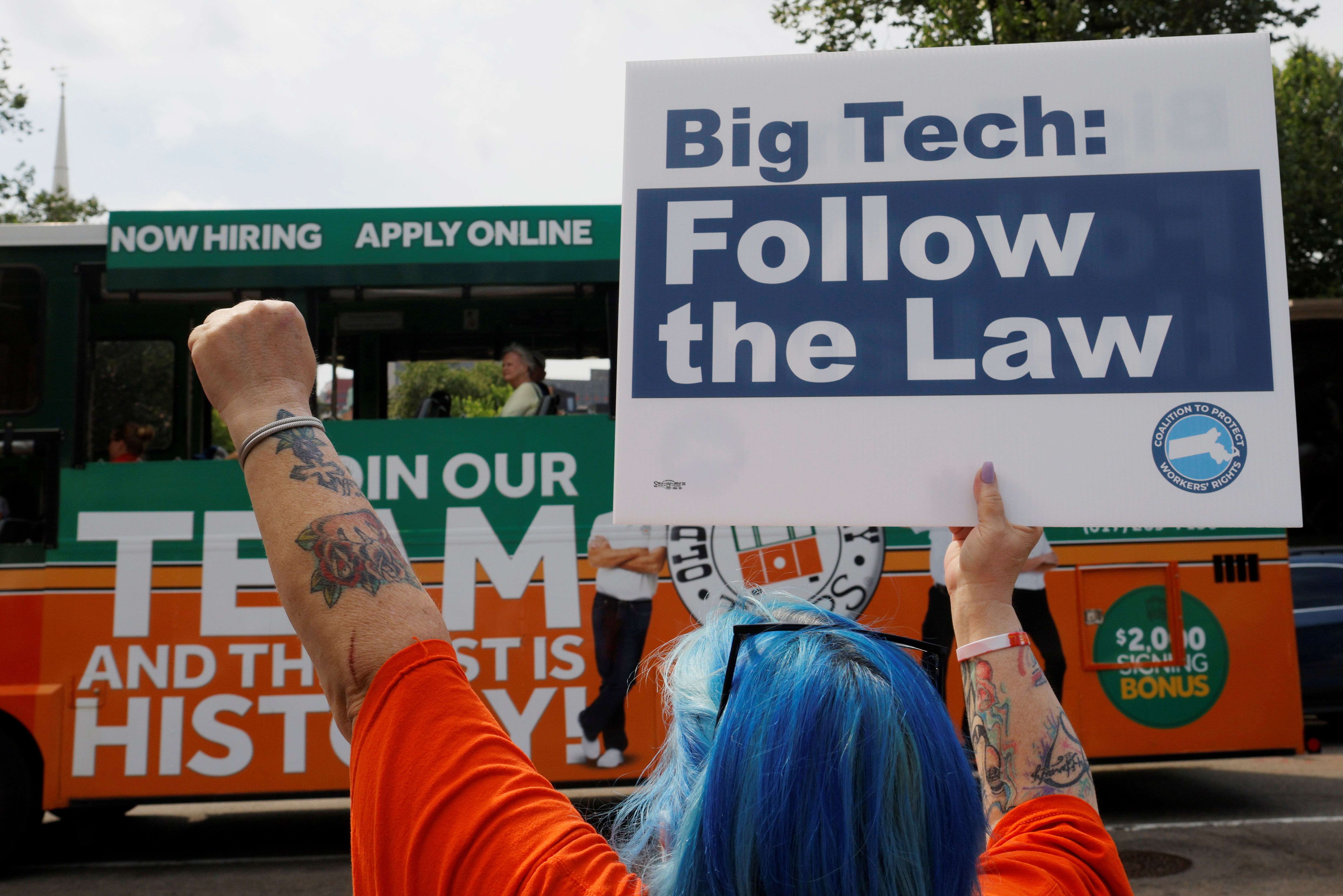 Mary Garcia, from New England United 4 Justice, gestures to a tour bus and holds a sign reading “Big Tech Follow the Law” at a demonstration opposing a ballot campaign by companies such has Uber, Lyft and Door Dash to exempt their companies from some labor laws outside the Massachusetts Statehouse in Boston, Massachusetts, U.S., June 22, 2021. 