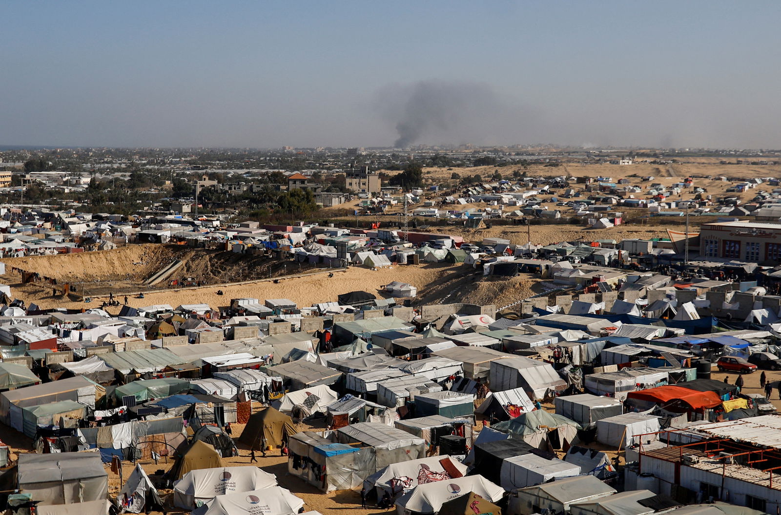 A general view of a tent camp housing displaced Palestinians, as smoke rises in the distance due to an Israeli ground operation in Khan Younis, amid the ongoing conflict between Israel and the Palestinian Islamist group Hamas, as seen Rafah in the southern Gaza Strip, January 22, 2024. 