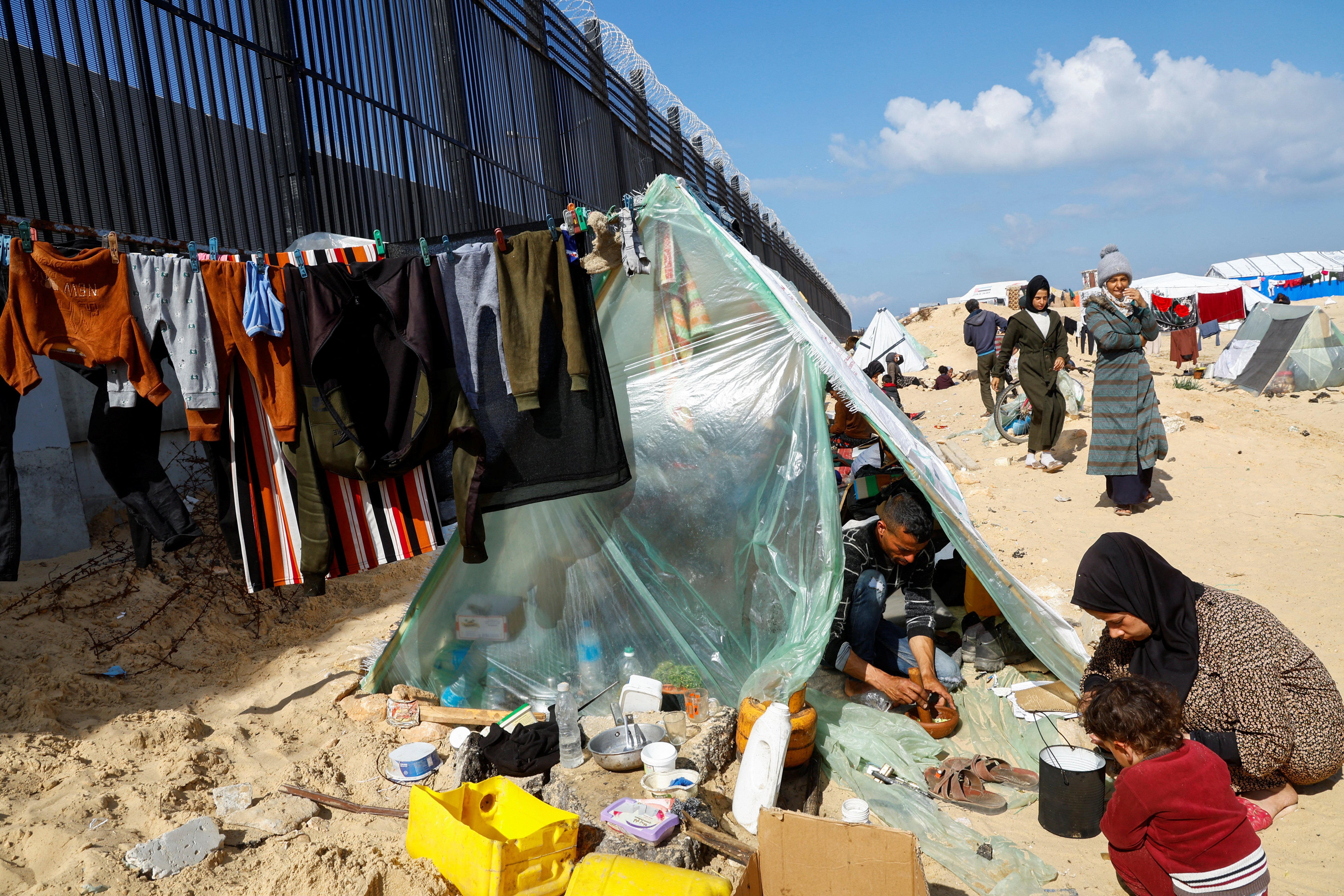 Displaced members of Palestinian Abu Mustafa family, who fled their house due to Israeli strikes, prepare food as they shelter at the border with Egypt, in Rafah in the southern Gaza Strip, February 10, 2024. 