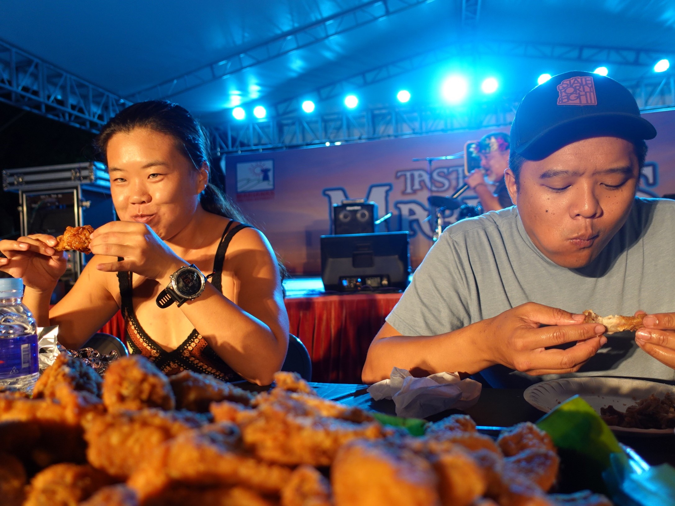 Michael Do, right, and Madge Gai chew their way to 1st  place and 3rd  place, respectively, in the Inas’ Fried Chicken Wing Eating Contest at the Taste of the Marianas International Food Festival in June 2023 on Saipan.   This year’s Taste of the Marianas will be held on May 4, 11, 18, and 25, 2024 at American Memorial Park.