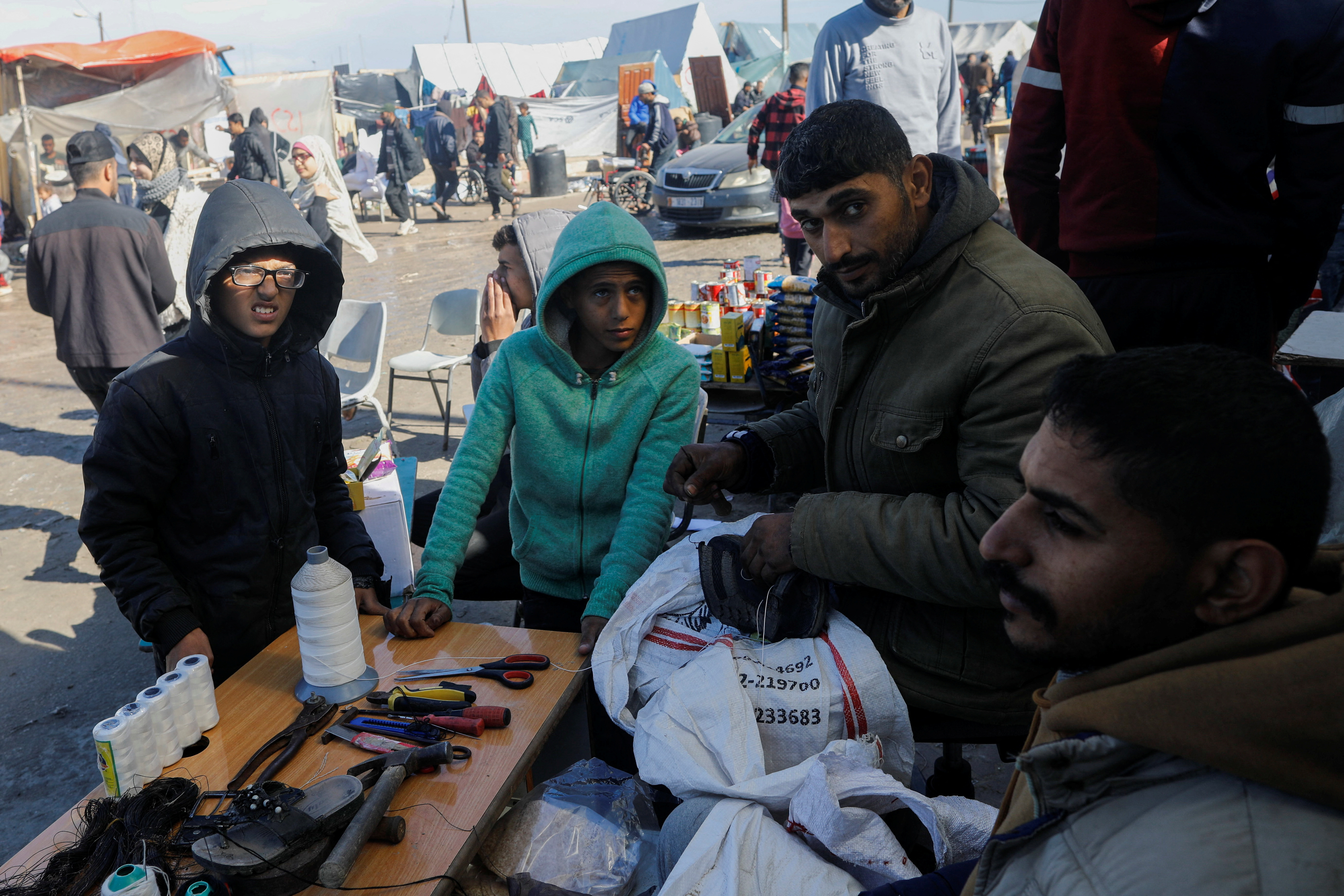 Displaced Palestinians, who fled their houses due to Israeli strikes, wait to get their slippers repaired by a cobbler, amid shortages of new footwear, in Rafah in the southern Gaza Strip January 31, 2024. 