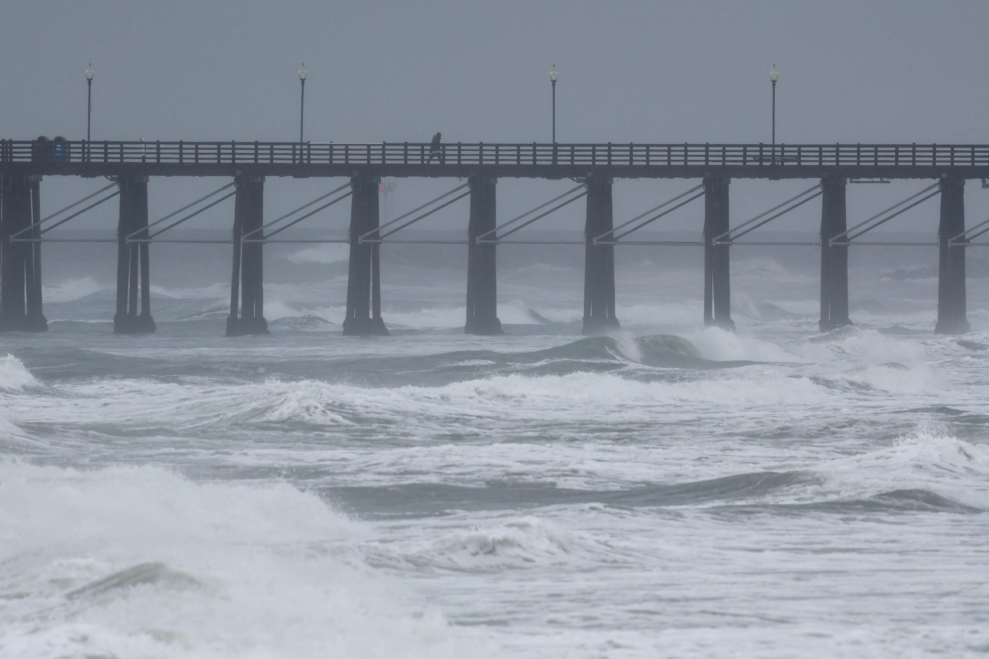 A person walk along a pier as an atmospheric river of rain continues to impact the weather in Oceanside, California, U.S., February 6, 2024. 