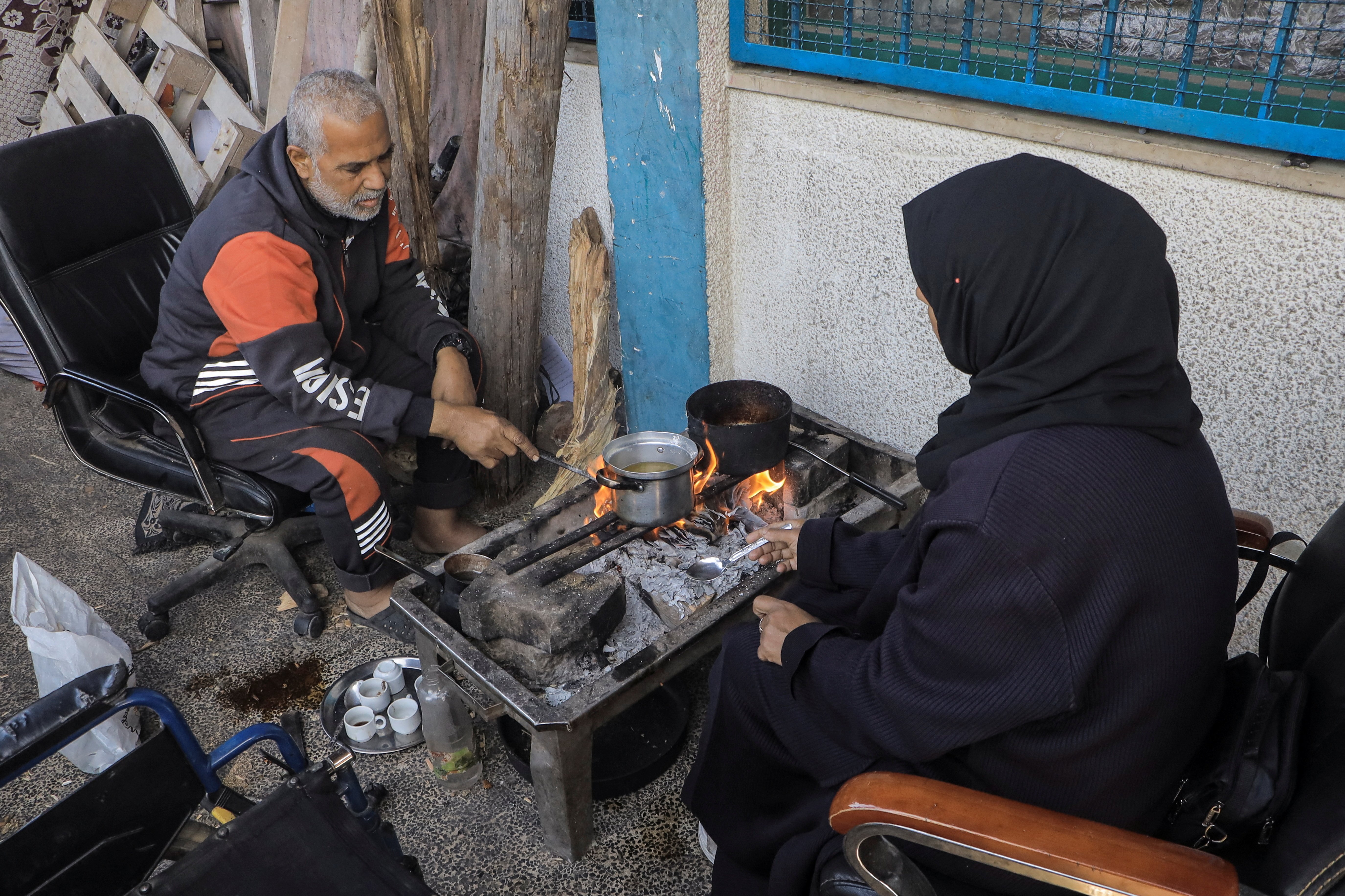 A Palestinian couple cooks on a fire, at a school where they shelter, amid the ongoing conflict between Israel and Hamas, in Jabalia refugee camp, in the northern Gaza Strip February 22, 2024. 