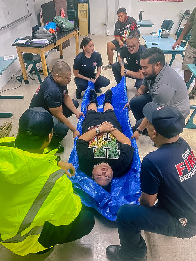Basic Disaster First-Aiders on Tinian utilize available materials to transport individuals requiring assistance. In this image, they used wood and a tarp for this purpose.