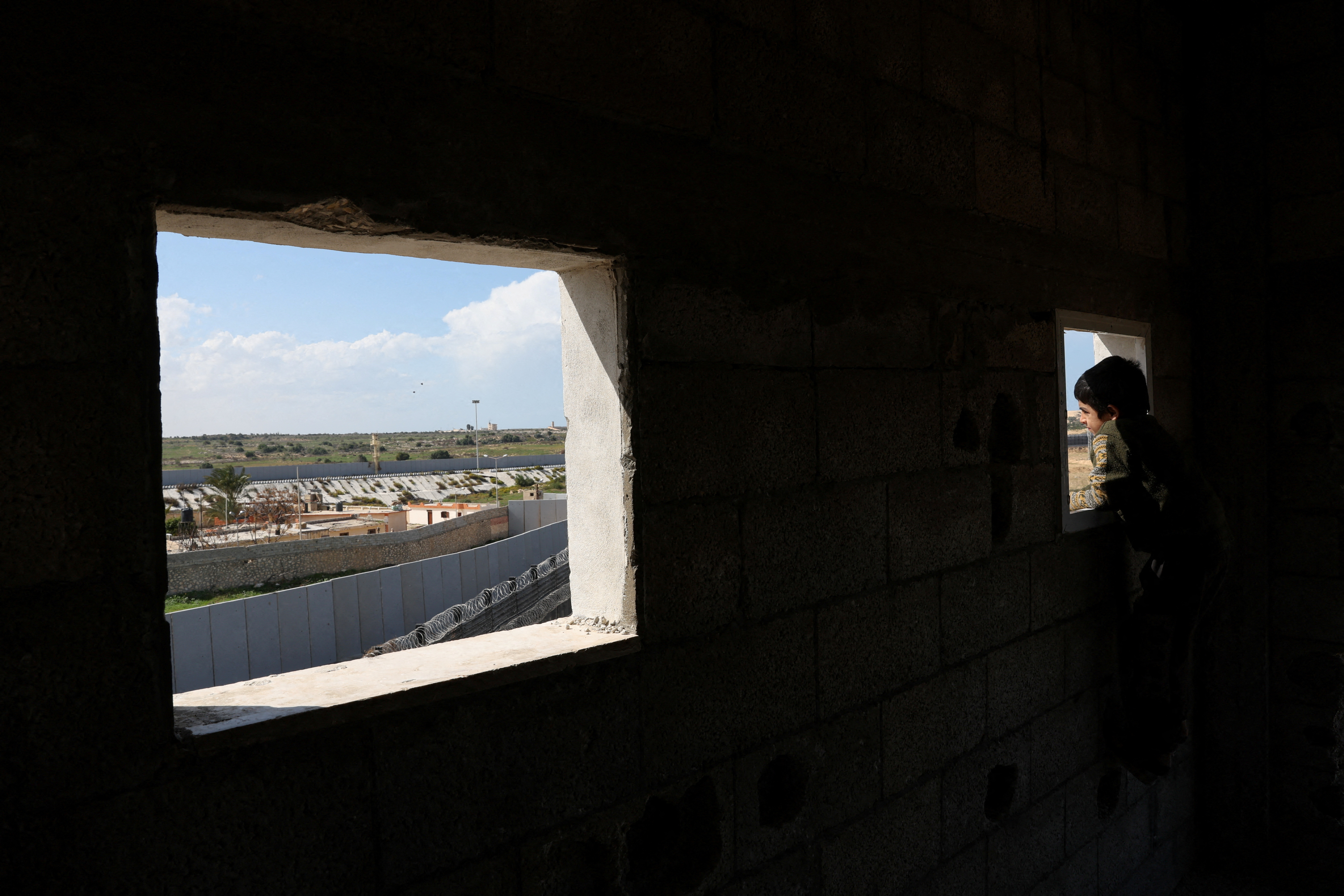 A displaced Palestinian child, who fled his house due to Israeli strikes looks through a window as he takes shelter at the border with Egypt, amid the ongoing conflict between Israel and the Palestinian Islamist group Hamas, in Rafah in the southern Gaza Strip, February 15, 2024. 