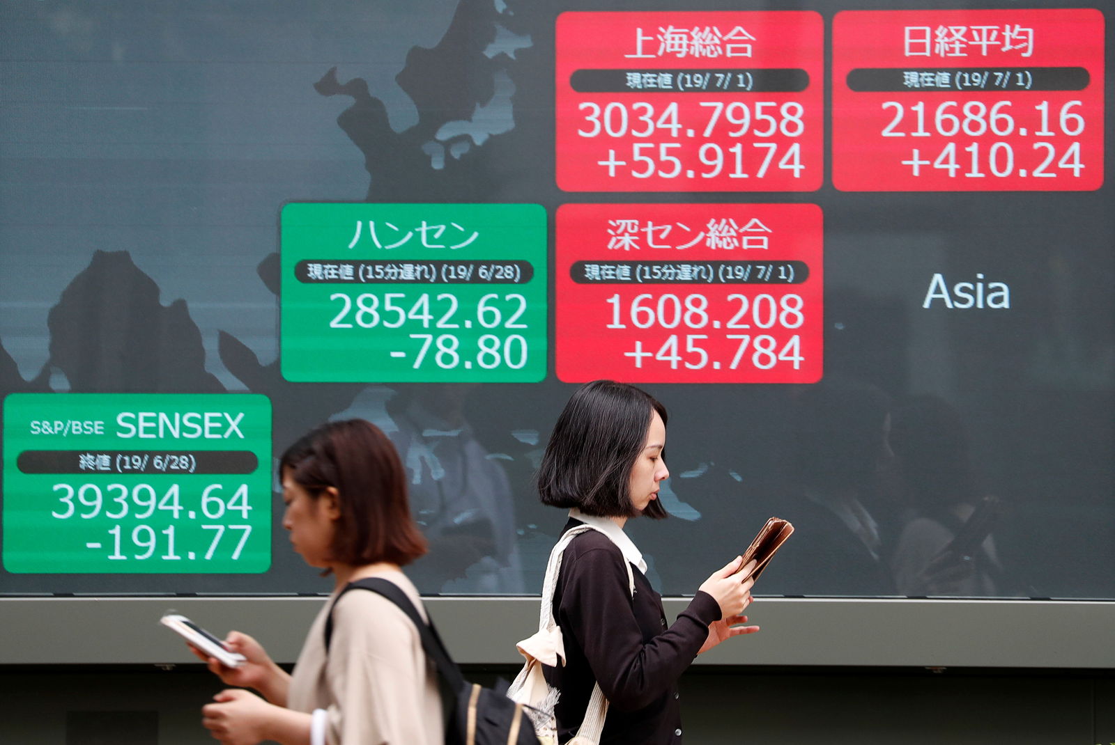 FILE PHOTO: Passerbys walk past an electric screen showing Asian markets indices outside a brokerage in Tokyo, Japan, July 1, 2019. 