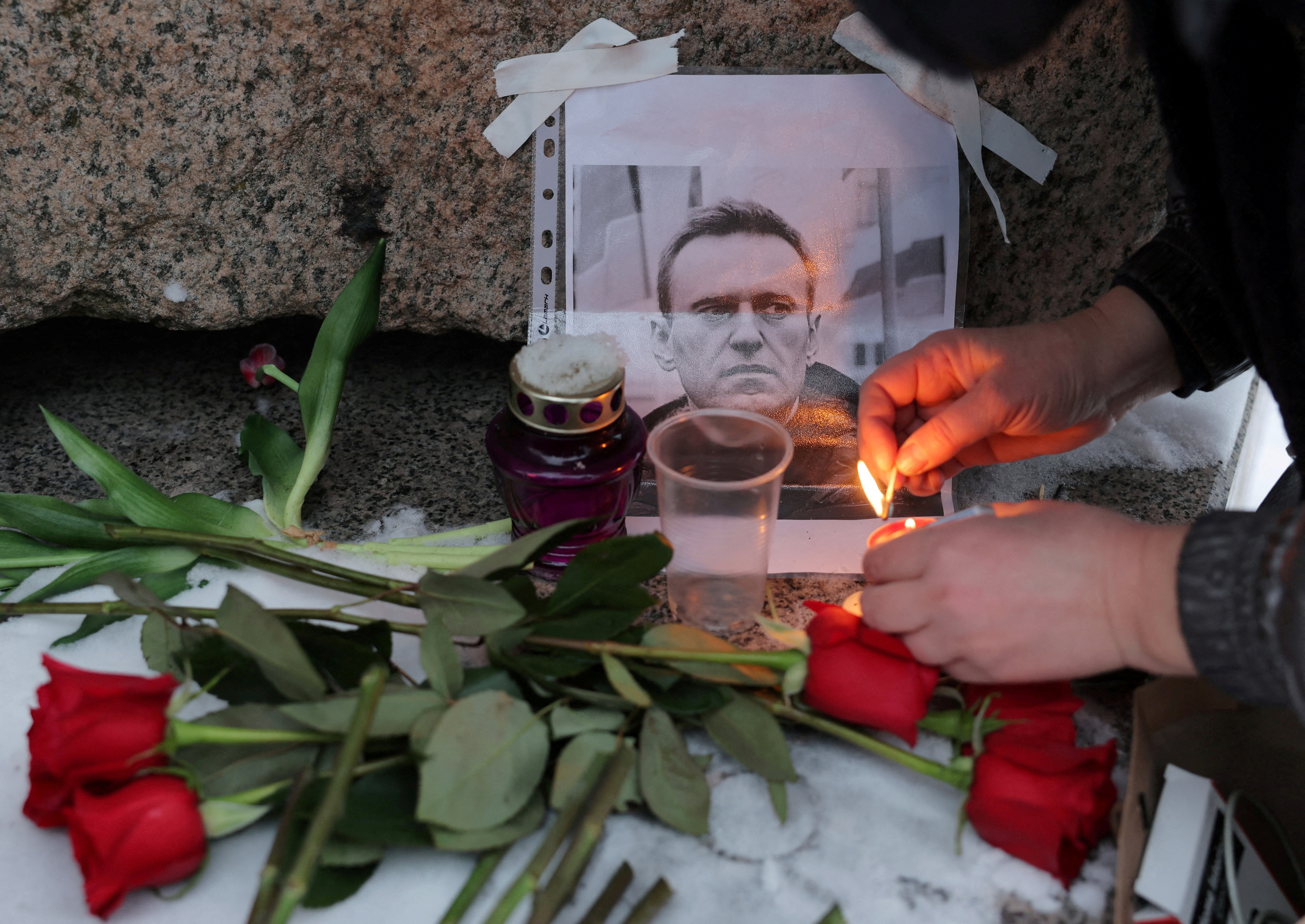 A person lights a candle next to a portrait of Russian opposition leader Alexei Navalny at the monument to the victims of political repression following Navalny's death, in Saint Petersburg, Russia, February 16, 2024. 