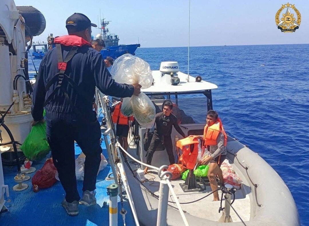 A member of Philippine Coast Guard personnel hands out supplies to the people onboard a rigid hull inflatable boat during a resupply mission in the South China Sea, March 23, 2024. 