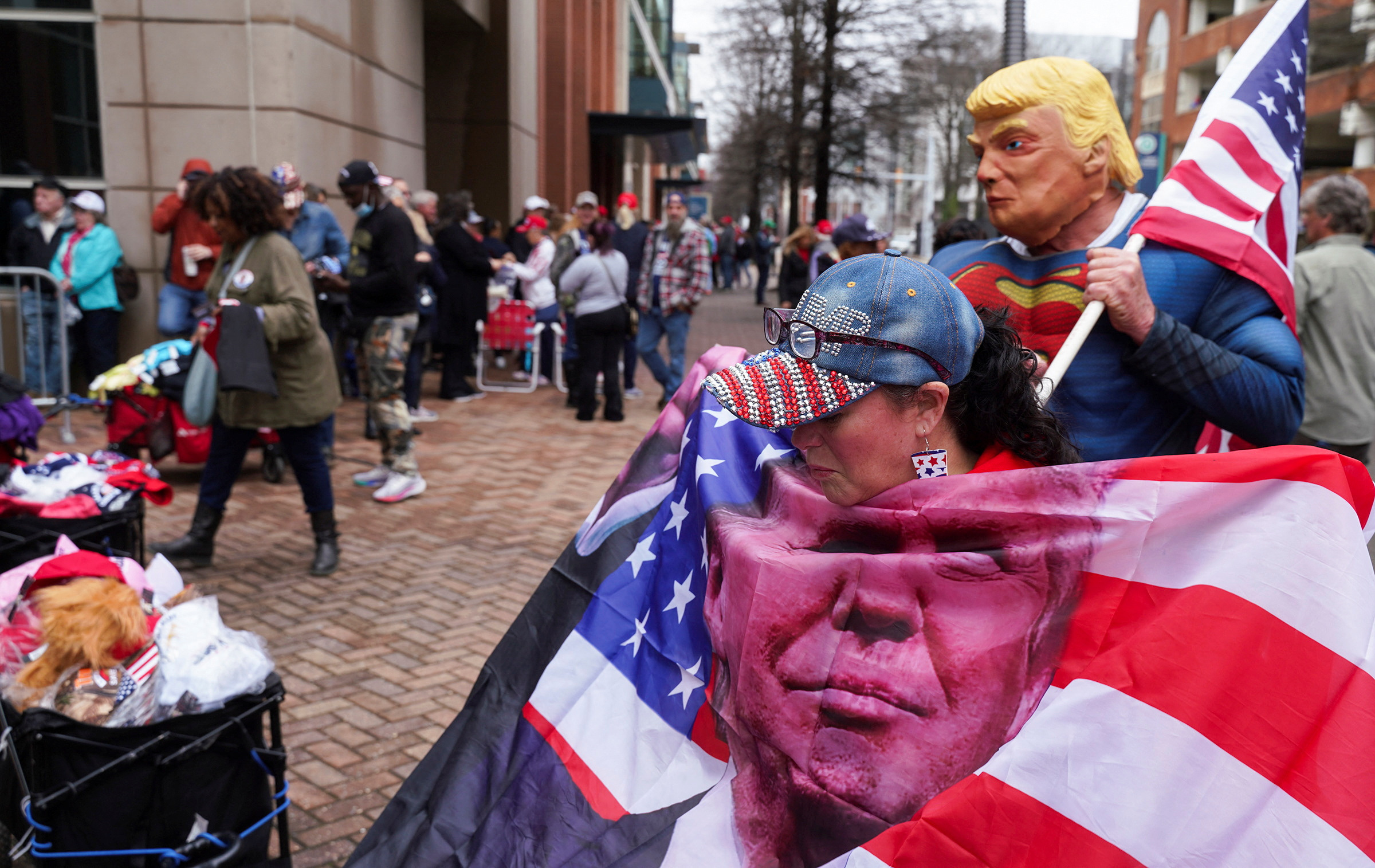 Jhonette Gamble looks at a U.S. flag with an image of Donald Trump, as "Super Trump", Kenny L’Heureux of Gloucester, VA, waits for the next person to pose with him, as Republican presidential candidate and former U.S. President Donald Trump holds a campaign rally tonight in Richmond, Virginia, U.S. March 2, 2024. 