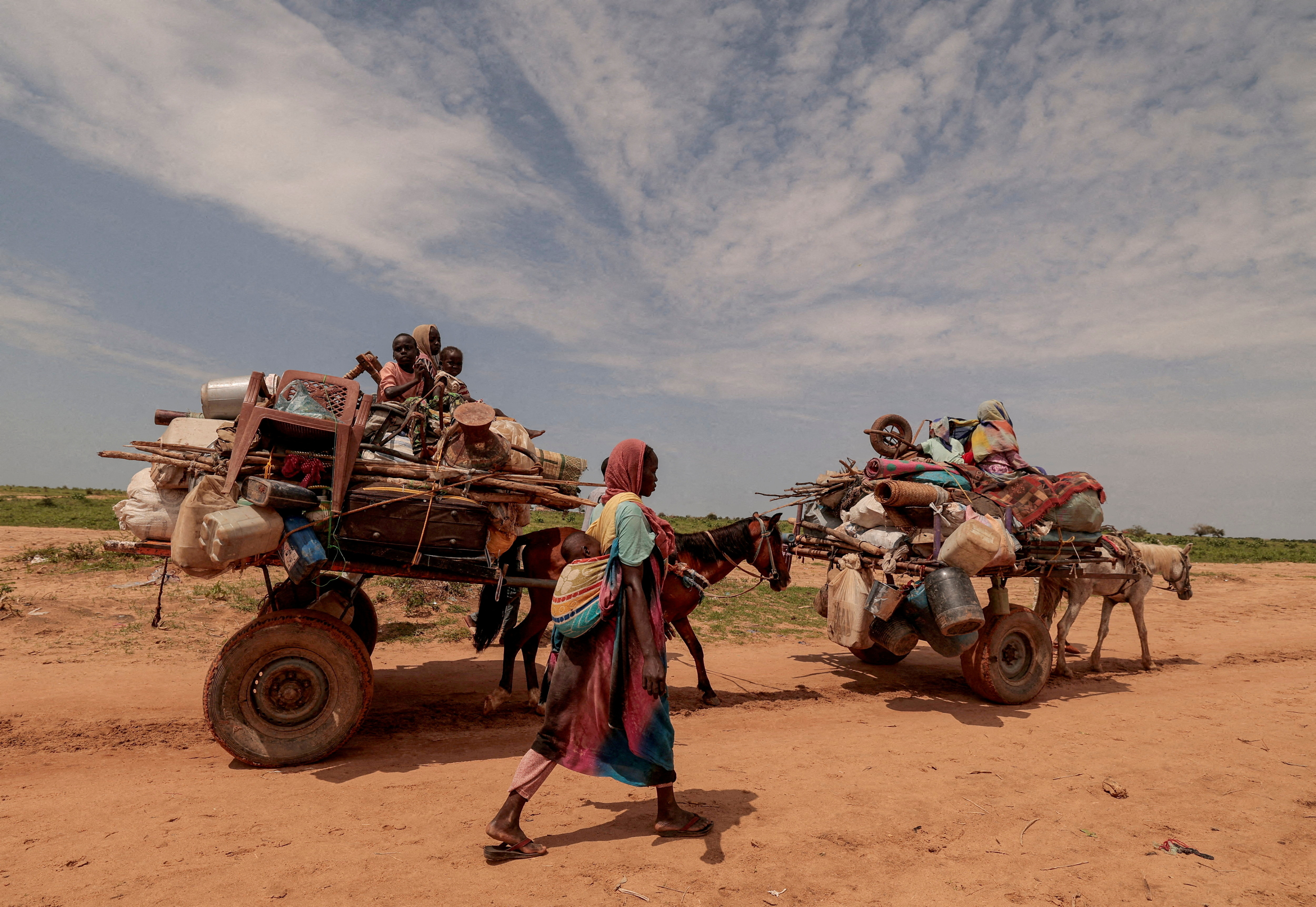 FILE PHOTO: A Sudanese woman, who fled the conflict in Murnei in Sudan's Darfur region, walks beside carts carrying her family belongings upon crossing the border between Sudan and Chad in Adre, Chad August 2, 2023. 