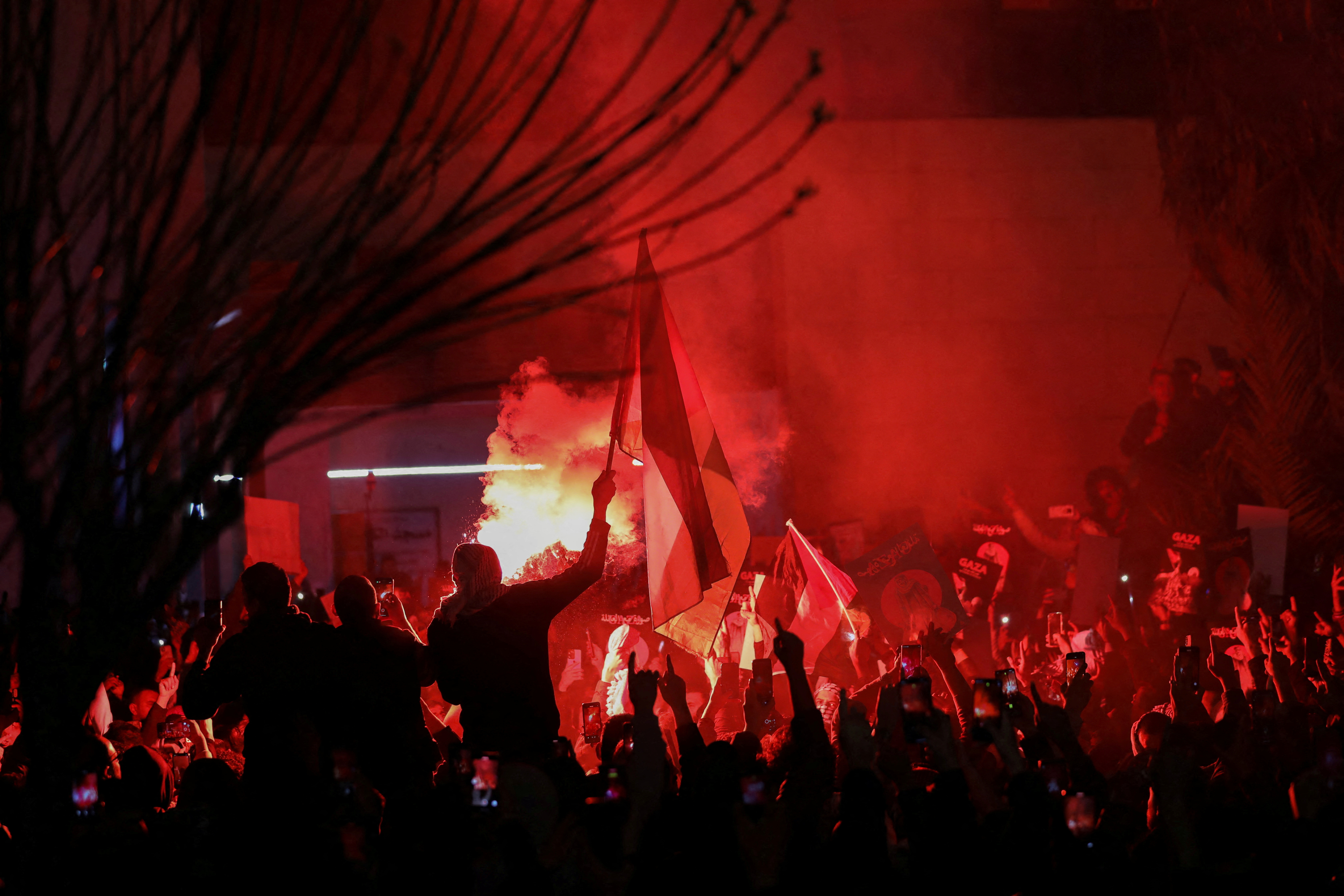 Demonstrators carry banners and flags as a flare burns during a protest in support of Palestinians in Gaza, amid the ongoing conflict between Israel and the Palestinian Islamist group Hamas, outside Al Kalouti mosque near the Israeli embassy in Amman, Jordan, March 27, 2024.