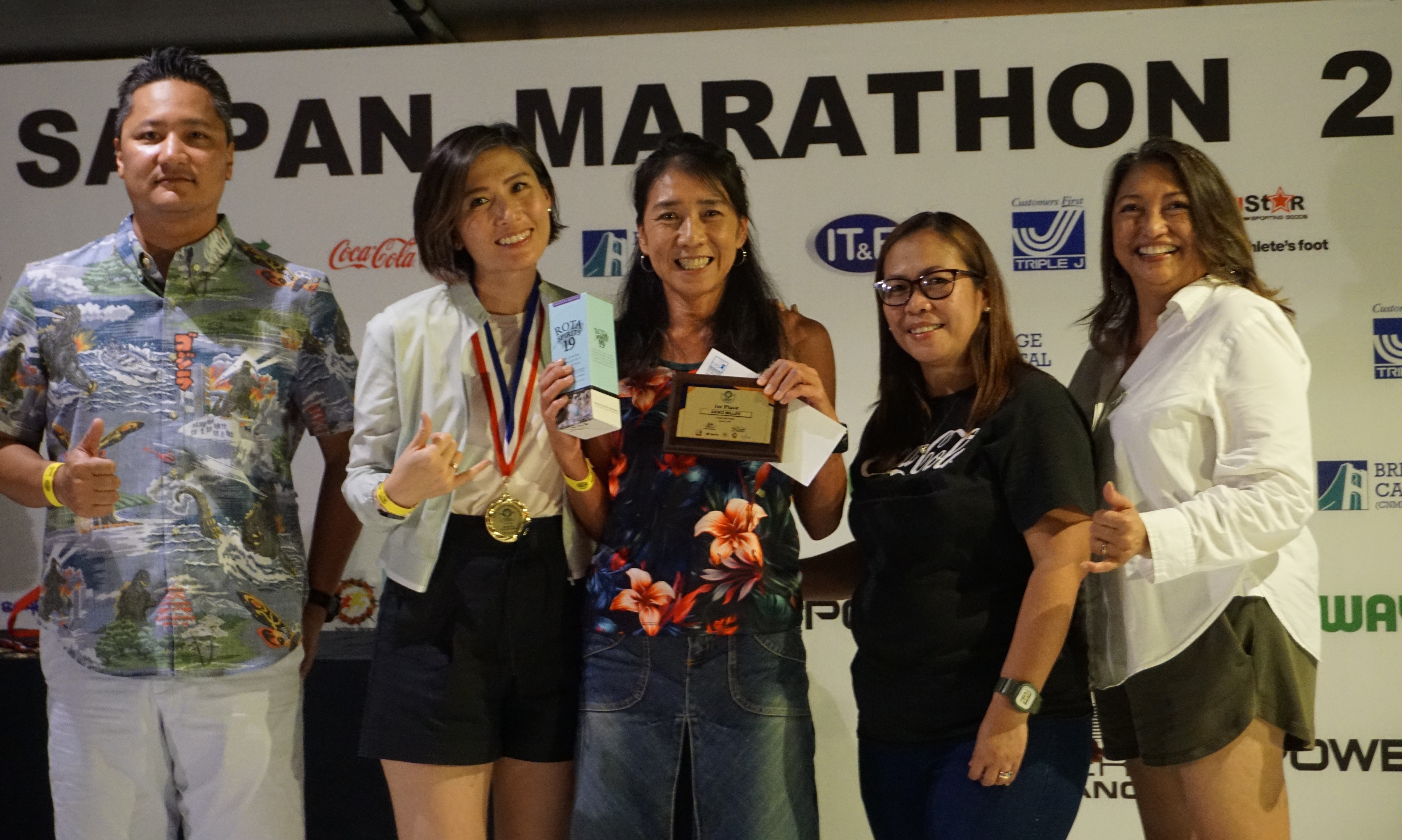 Akiko Miller, center, holds her 1st place plaque and other prizes for finishing first in the women’s division of the Saipan Marathon’s 10K event as she poses for a photo with Marianas Visitors Authority Managing Director Christopher Concepcion, Skechers representative Jennifer Tan, Coca-Cola representative Aileen Benavidez, and MVA acting Chair Gloria Cavanagh during the awards banquet at the Hyatt Regency Saipan on Saturday.