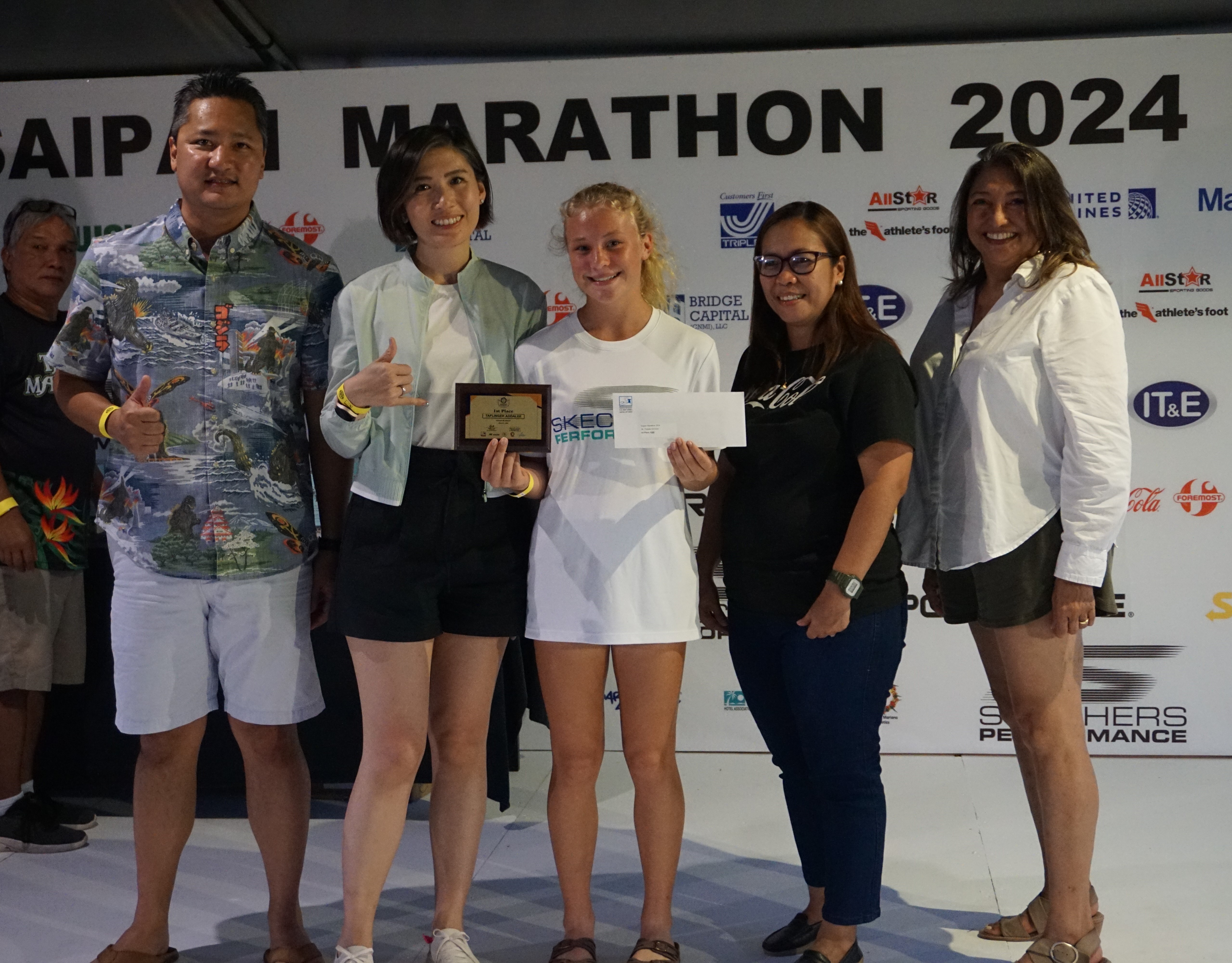 Addalee Taflinger, center, holds her 1st place plaque and her other prize for topping the women’s division of the Saipan Marathon’s 5K event as she poses for a photo with Marianas Visitors Authority Managing Director Christopher Concepcion, Skechers representative Jennifer Tan, Coca-Cola representative Aileen Benavidez, and MVA acting Chair Gloria Cavanagh during the awards banquet at the Hyatt Regency Saipan on Saturday.
