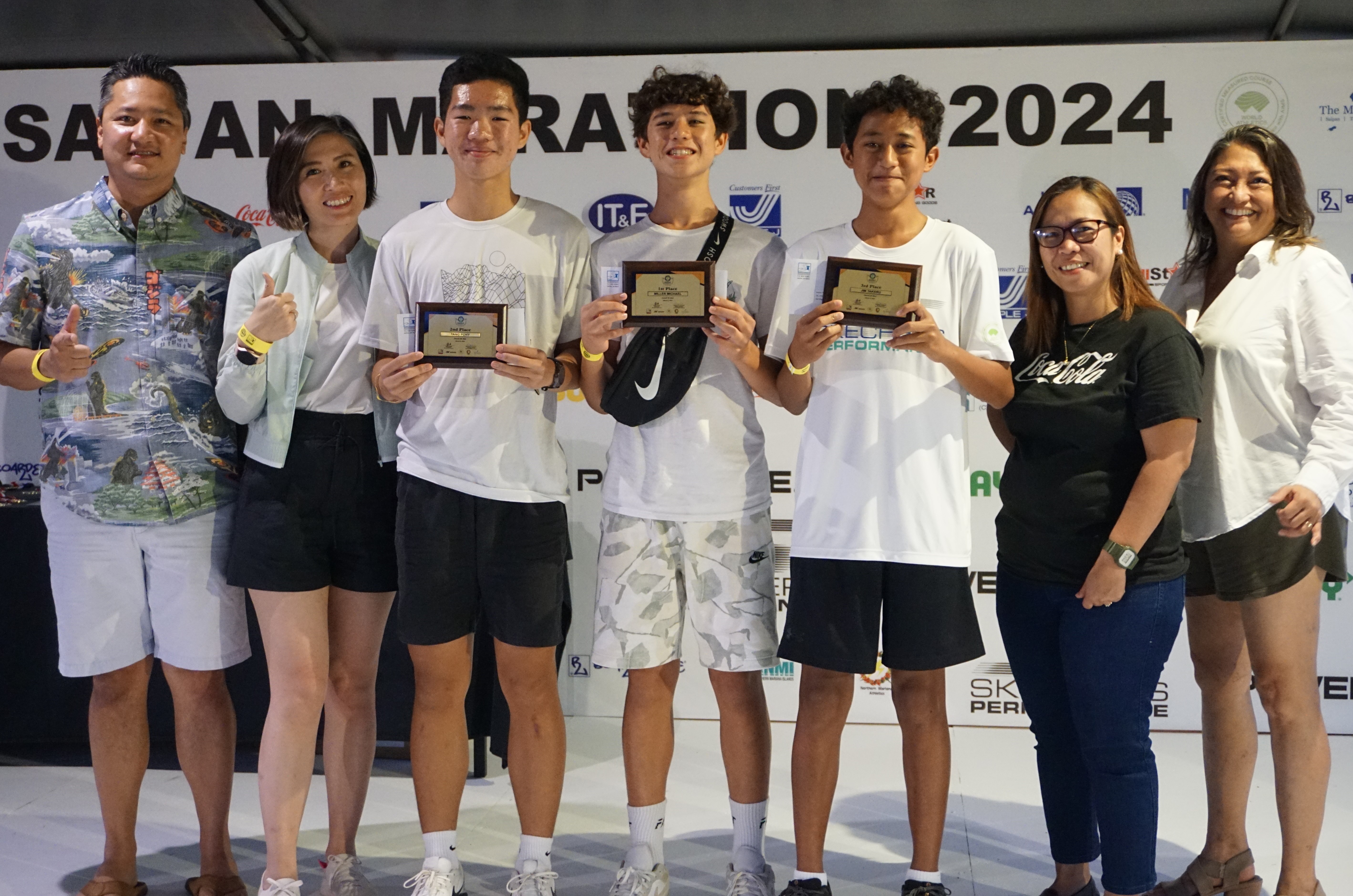Marianas High School students Pony Tang, Michael Miller, and Jim Takeru, center, hold their 1st, 2nd, and 3rd place plaques in the 5K event of the Saipan Marathon as they pose for a photo with Marianas Visitors Authority Managing Director Christopher Concepcion, Skechers representative Jennifer Tan, Coca-Cola representative Aileen Benavidez, and MVA acting Chair Gloria Cavanagh during the awards banquet at the Hyatt Regency Saipan on Saturday. 