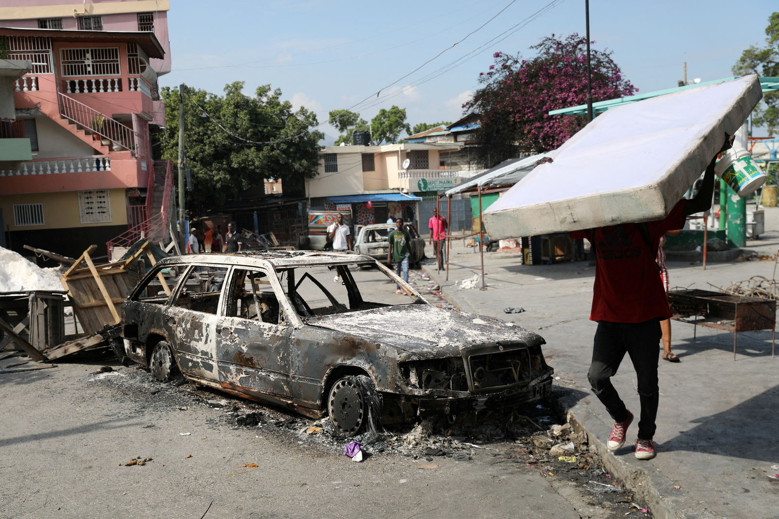 FILE PHOTO: A resident carries a mattress while walking by a car burnt by gang members, as the government said it would extend a state of emergency for another month after an escalation in violence from gangs seeking to oust the Prime Minister Ariel Henry, in Port-au-Prince, Haiti, March 7, 2024. REUTERS/Ralph Tedy Erol/File Photo