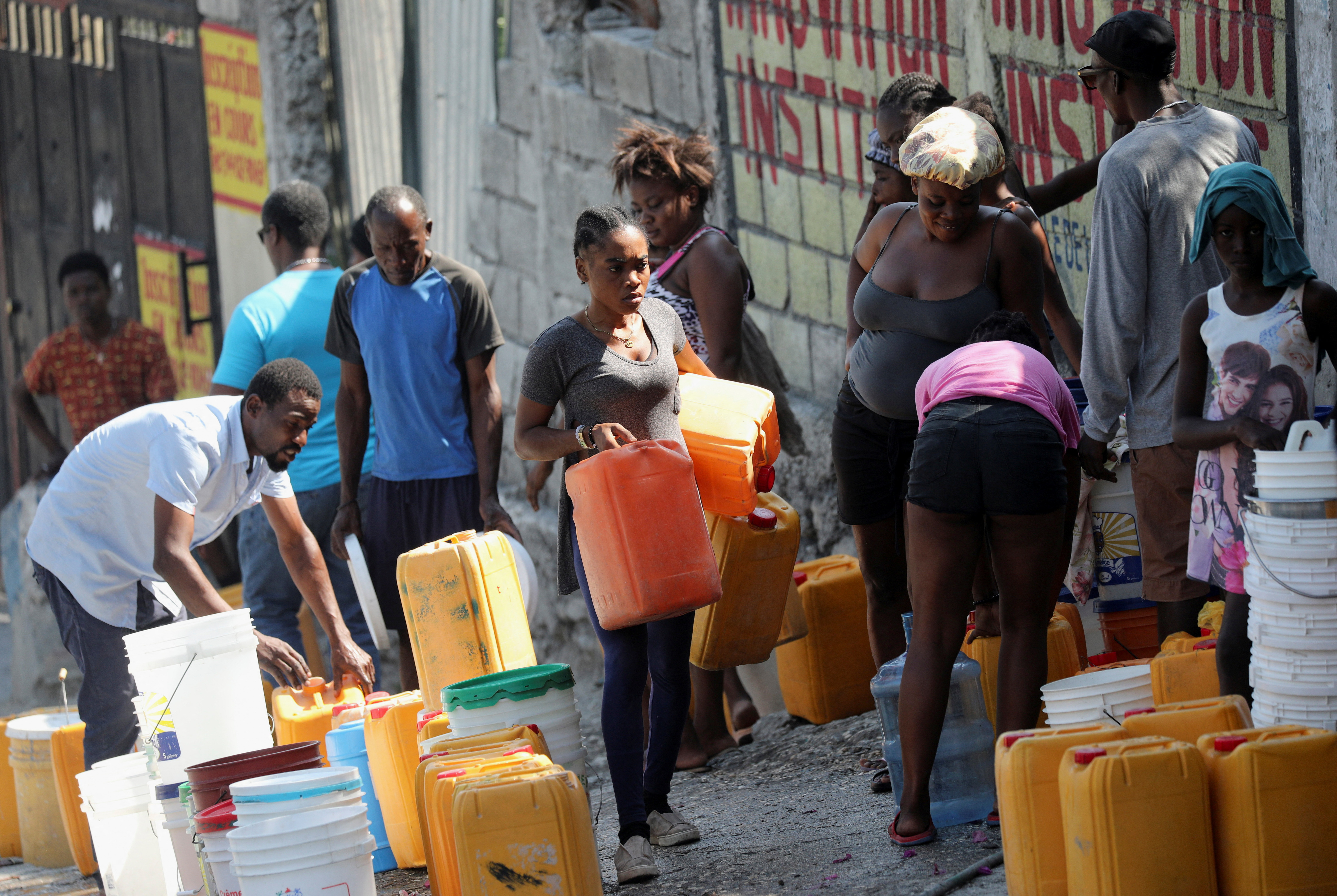 People wait along a street to collect water in buckets and containers after Haiti's Prime Minister Ariel Henry pledged to step down following months of escalating gang violence, in Port-au-Prince, Haiti March 12, 2024. 