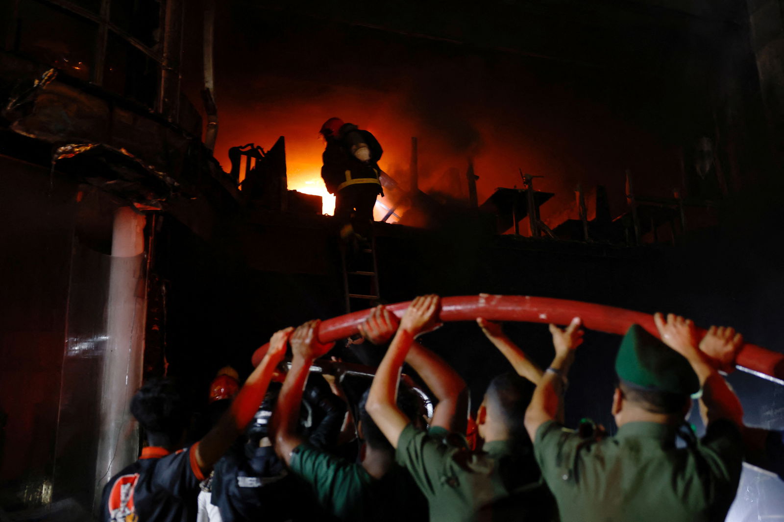 Volunteers carry a water pipe as firefighters spray water to douse the fire after a fire that broke out in a multi-storey building in Dhaka, Bangladesh, February 29, 2024. 
