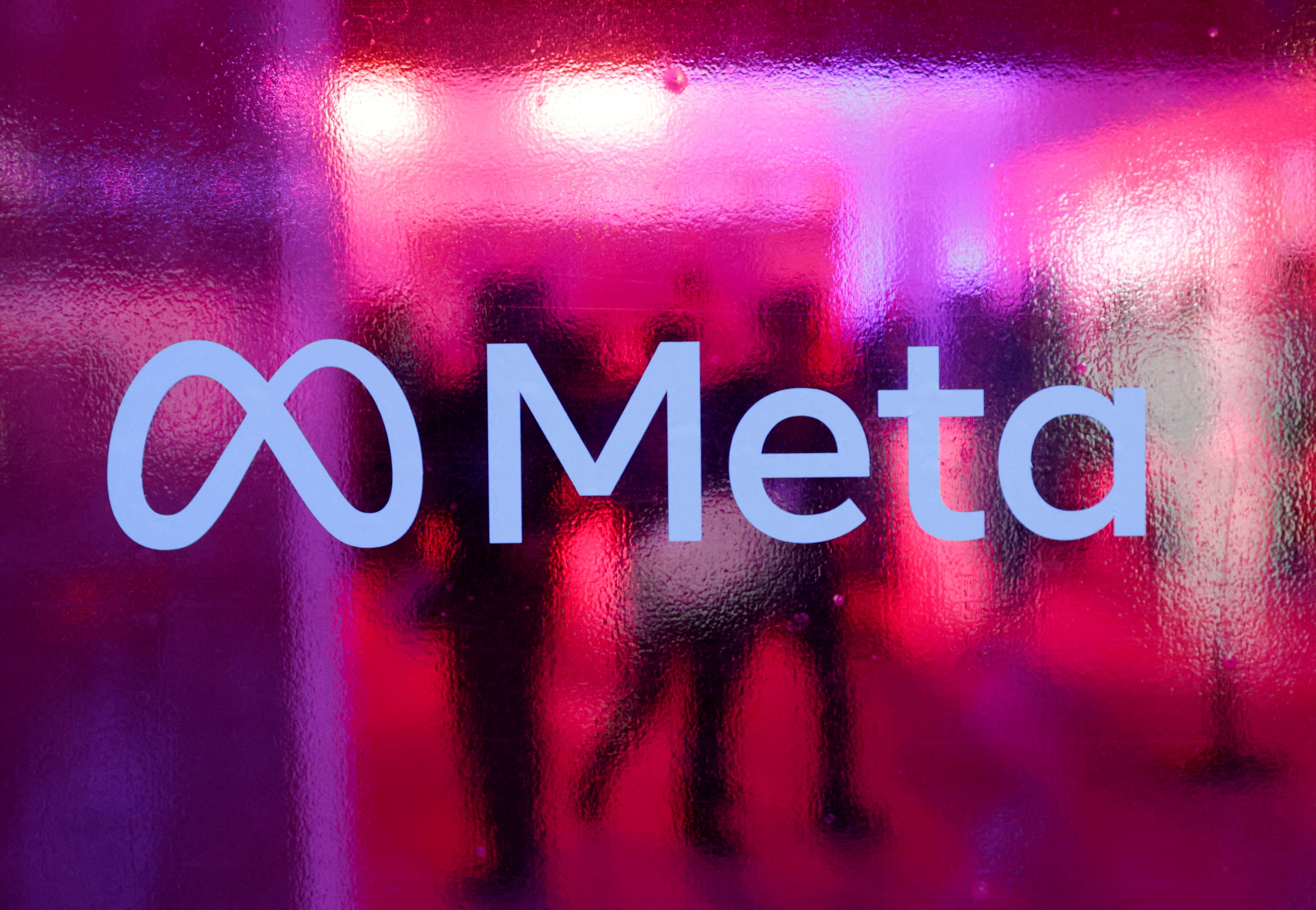 FILE PHOTO: People walk behind Meta Platforms logo during a conference in Mumbai, India, September 20, 2023. 