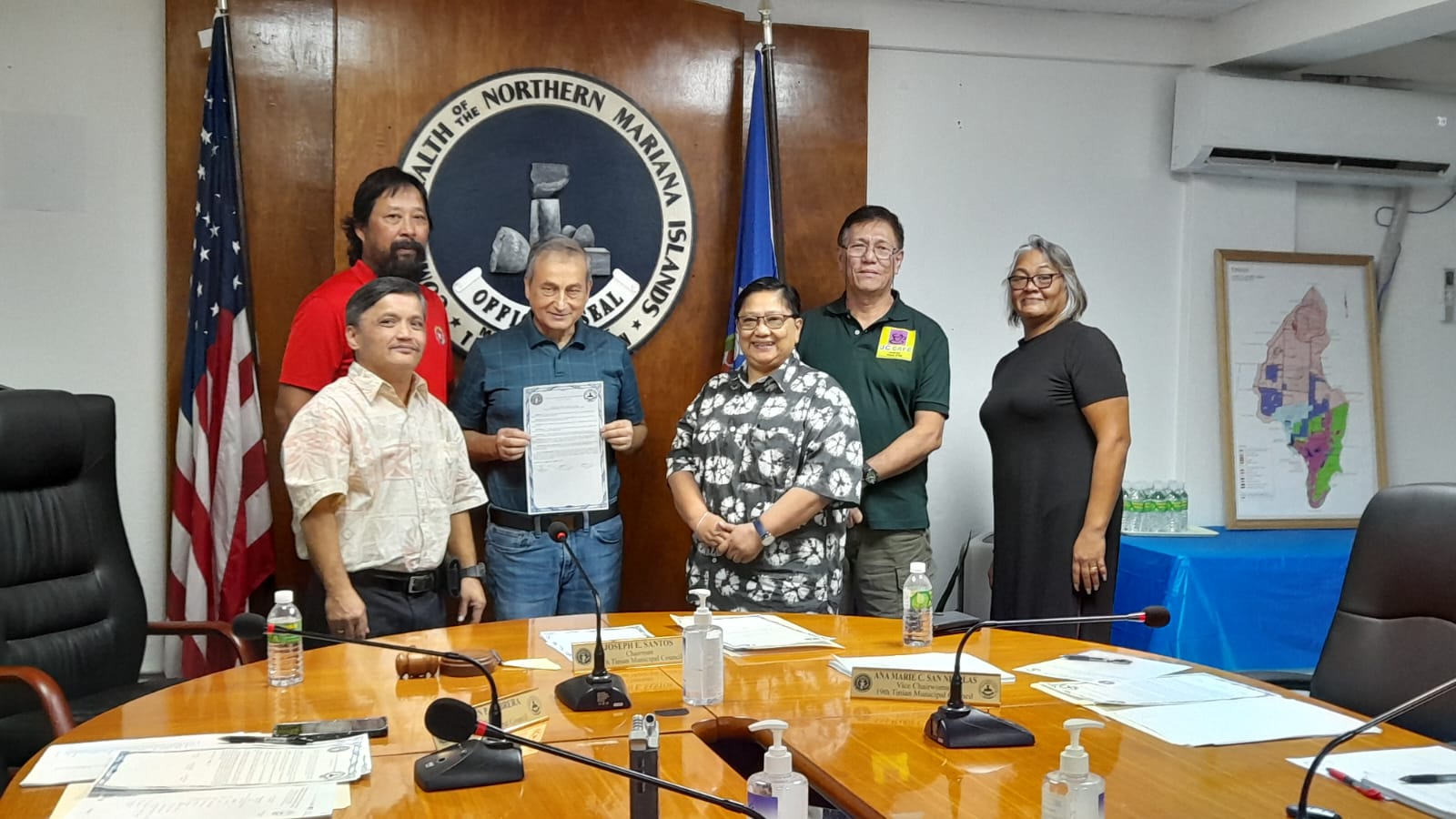 JC Café owner Neal Eisgrou holds a copy of a Tinian Municipal Council  resolution as he poses for a photo with the council chairman, Joseph E. Santos, second left, council secretary Estevan Cabrera, left, JC Café operations manager Lot Bunao, third right, JC Café accountant Edgar Tirona, second right, and council vice chair Ana Marie C. San Nicolas in the Tinian Mayor's Office conference room on Friday.