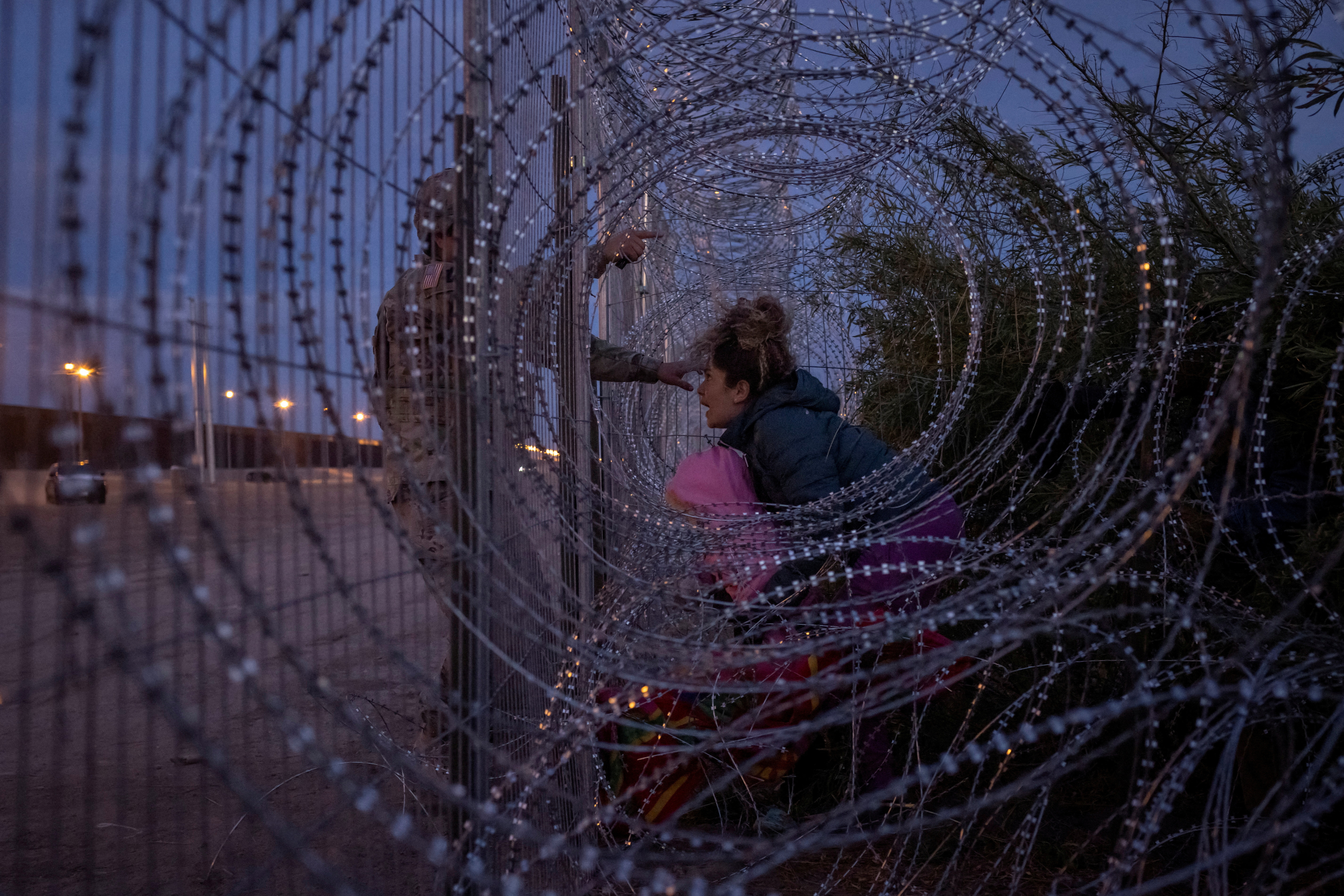 Eliana, 22, a migrant from Venezuela, holds her three-year-old daughter Chrismarlees as she shouts towards an Army National Guard soldier after he halts her from breaching a razor wire-laden fence along the bank of the Rio Grande river in El Paso, Texas, U.S., March 26, 2024. 