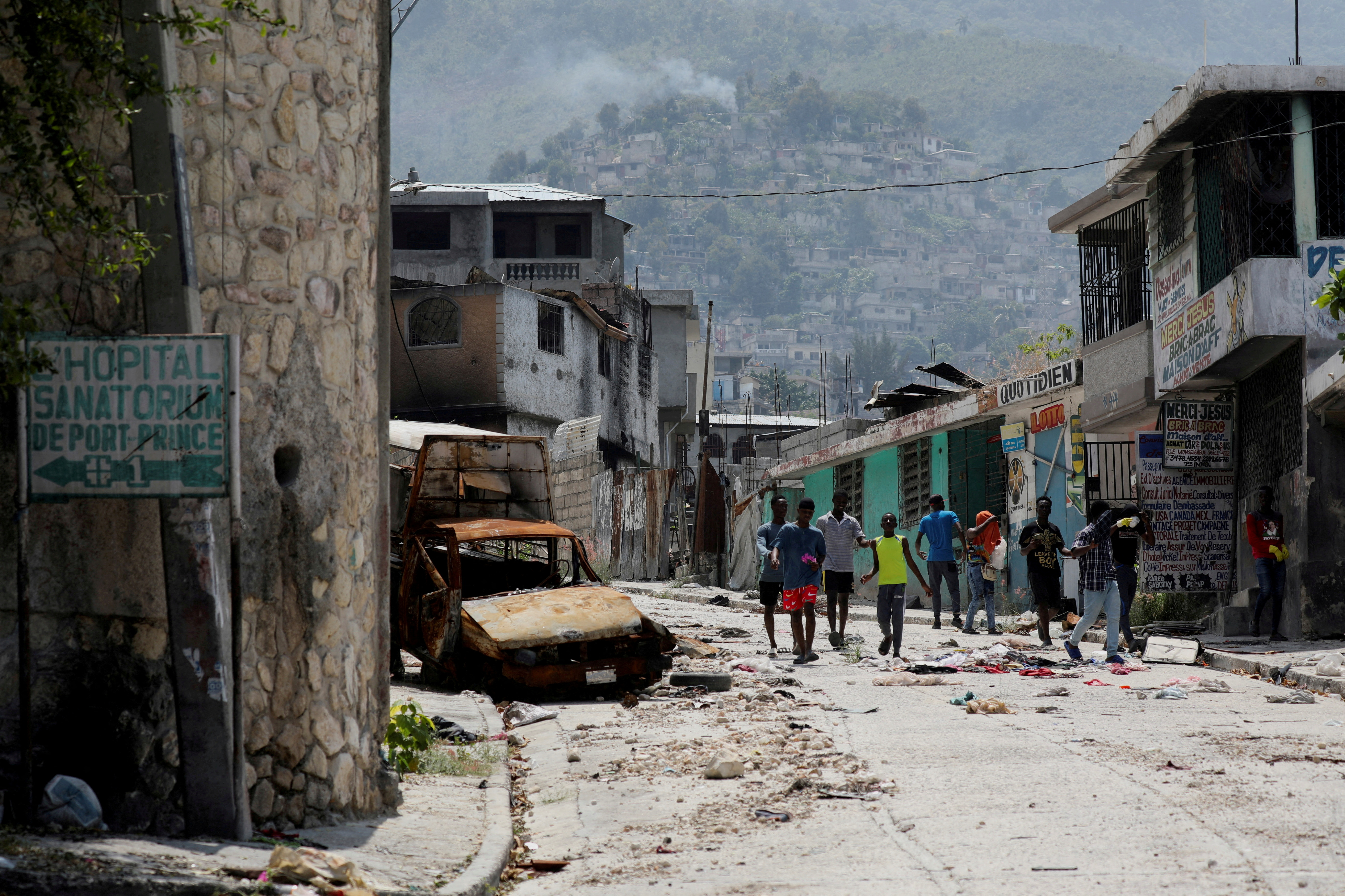 FILE PHOTO: People walk past a damaged car in the Carrefour Feuilles neighborhood, which was deserted due to gang violence, in Port-au-Prince, Haiti March 19, 2024. 