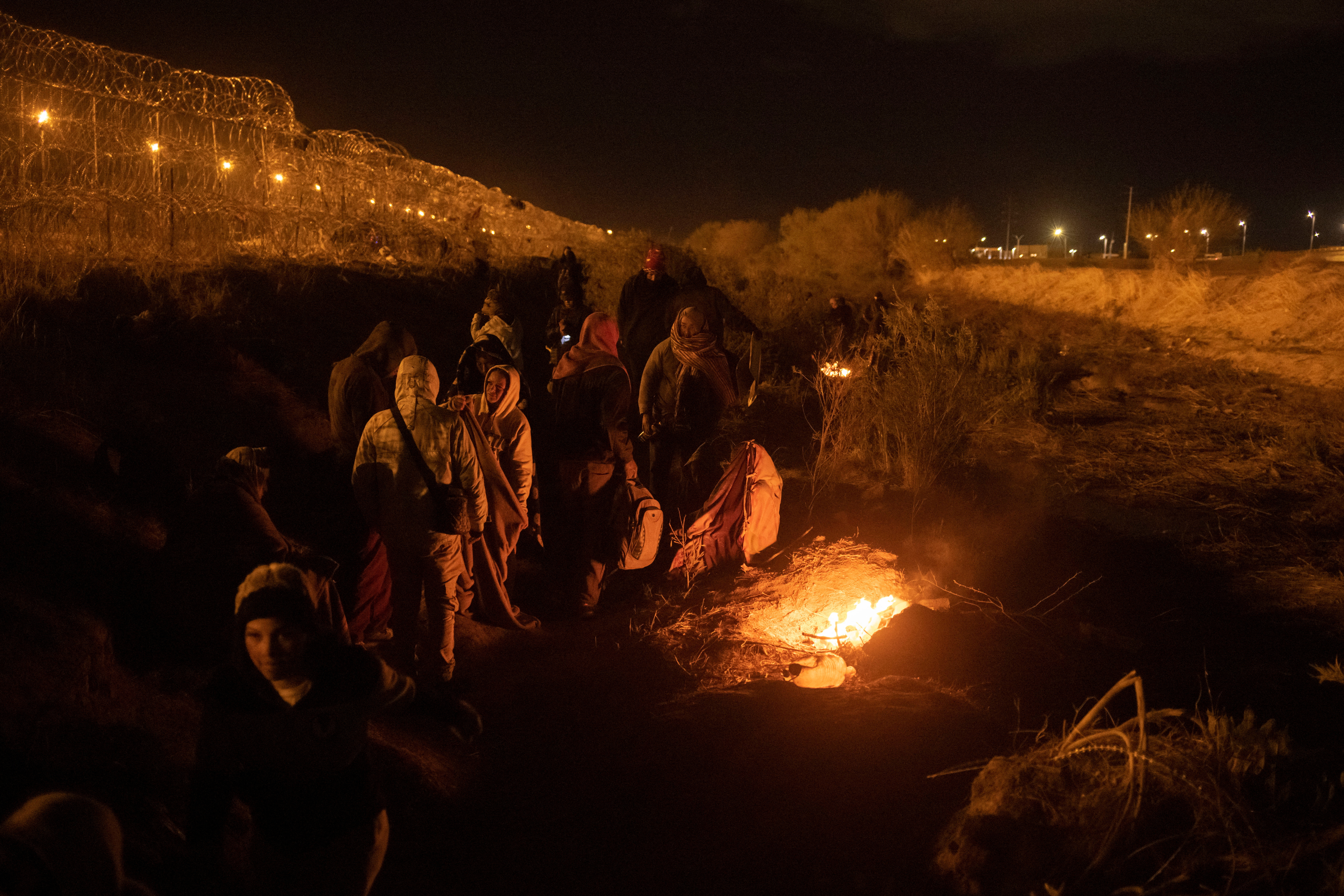 Migrants from South and Central America huddle near fire as they search for an entry point into the United States past a razor wire-laden fence along the bank of the Rio Grande river in El Paso, Texas, U.S., March 26, 2024. 