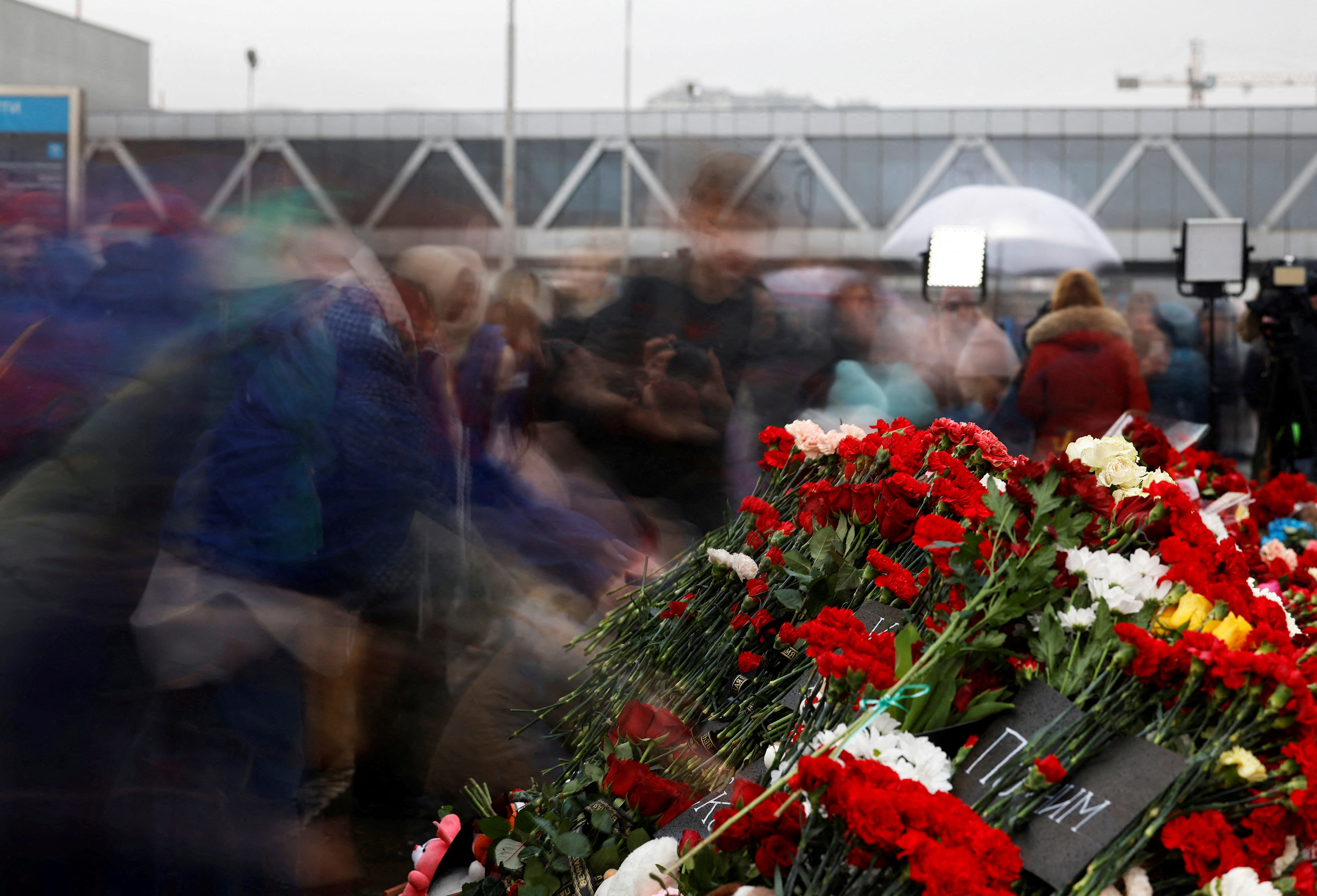 People lay flowers at a makeshift memorial to the victims of a shooting attack, set up outside the Crocus City Hall concert venue in the Moscow Region, Russia, March 24, 2024. Picture taken with a slow shutter speed. 