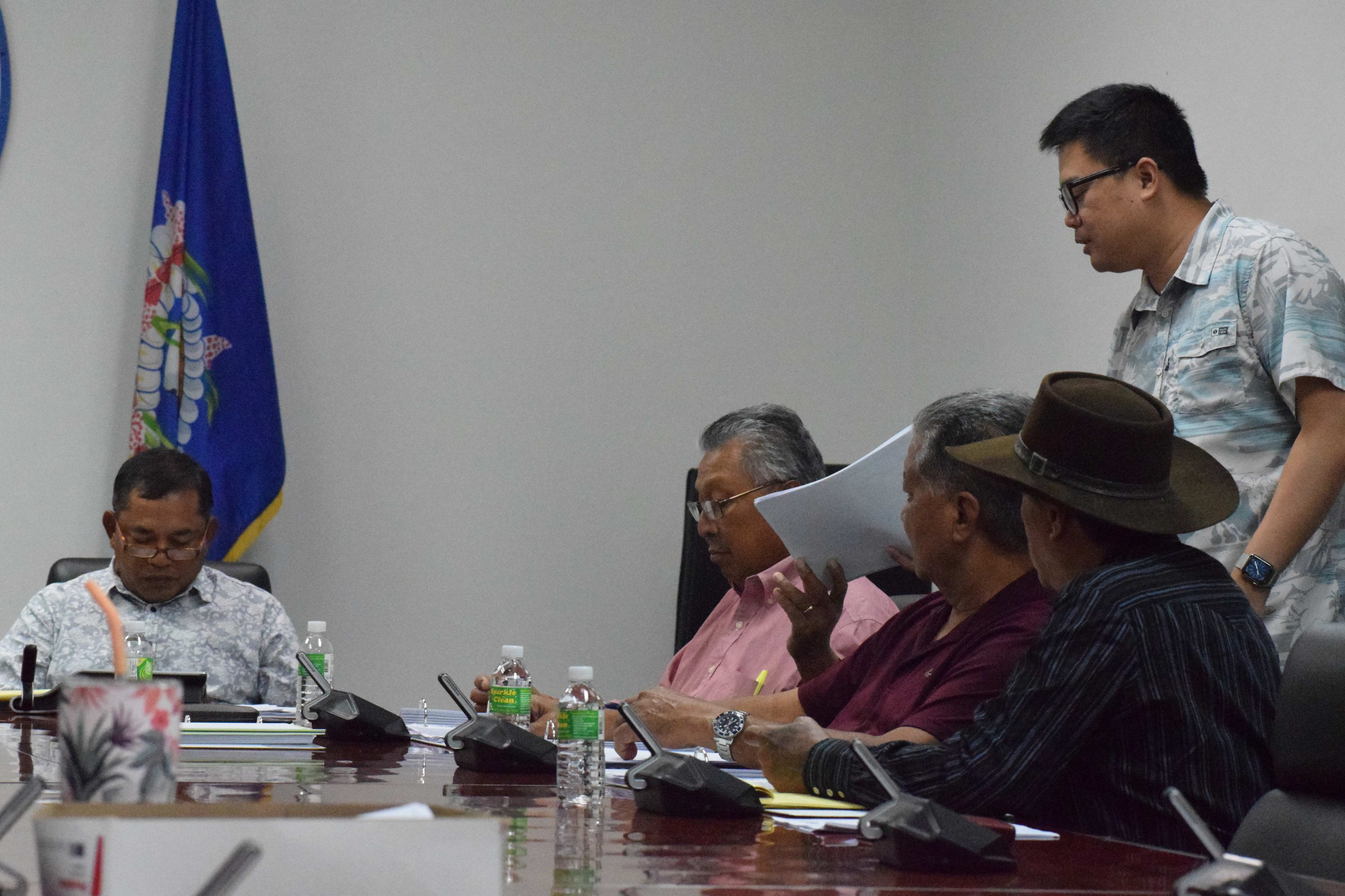 Imperial Pacific International Director Howyo Chi, right standing, hands copies of the proposed settlement terms to members of the Commonwealth Casino Commission.