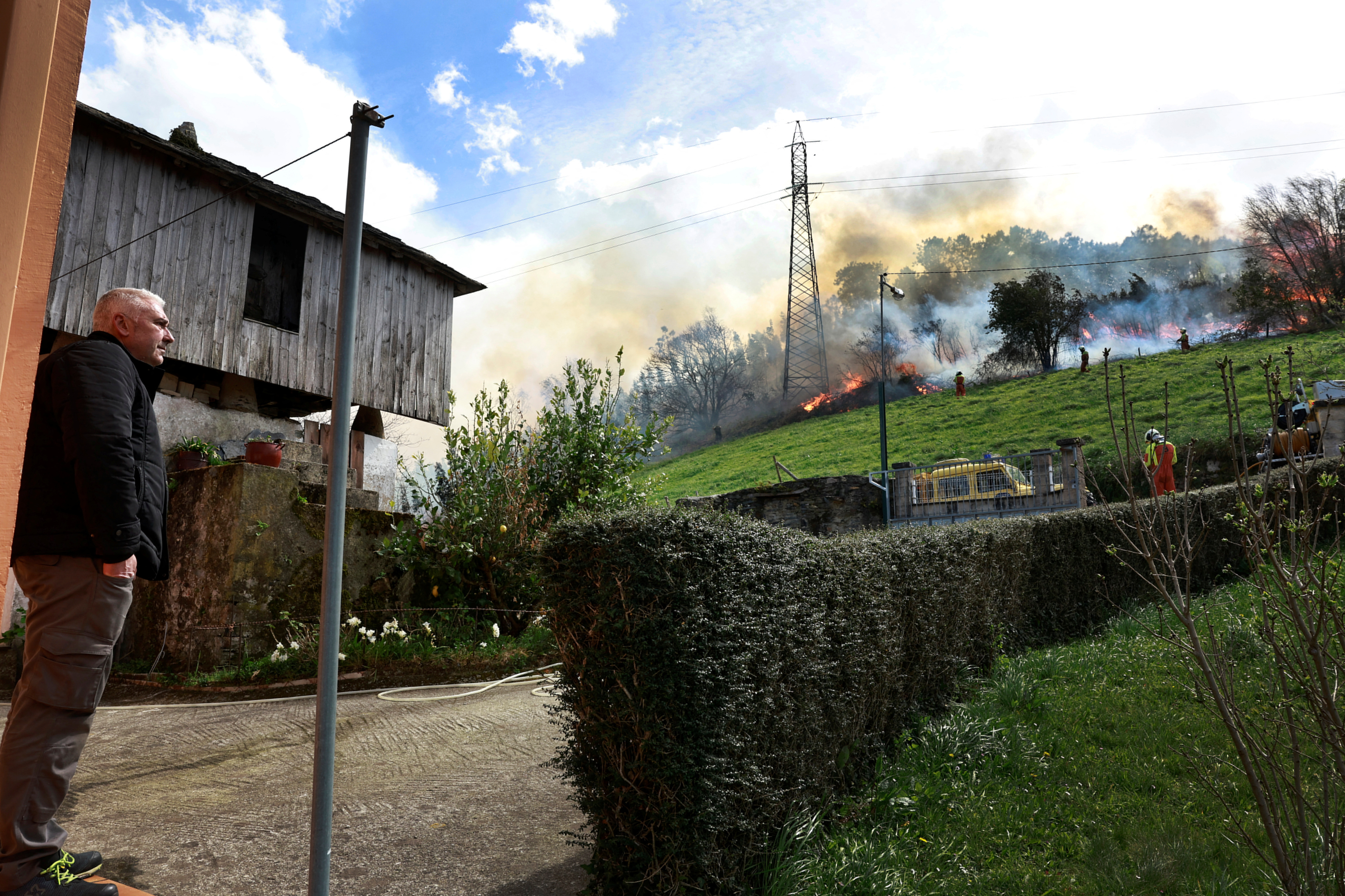 A homeowner observes firefighters tackling a blaze near the village of Setienes during an outbreak of wildfires in northern Spain's Asturias region, March 31, 2023.