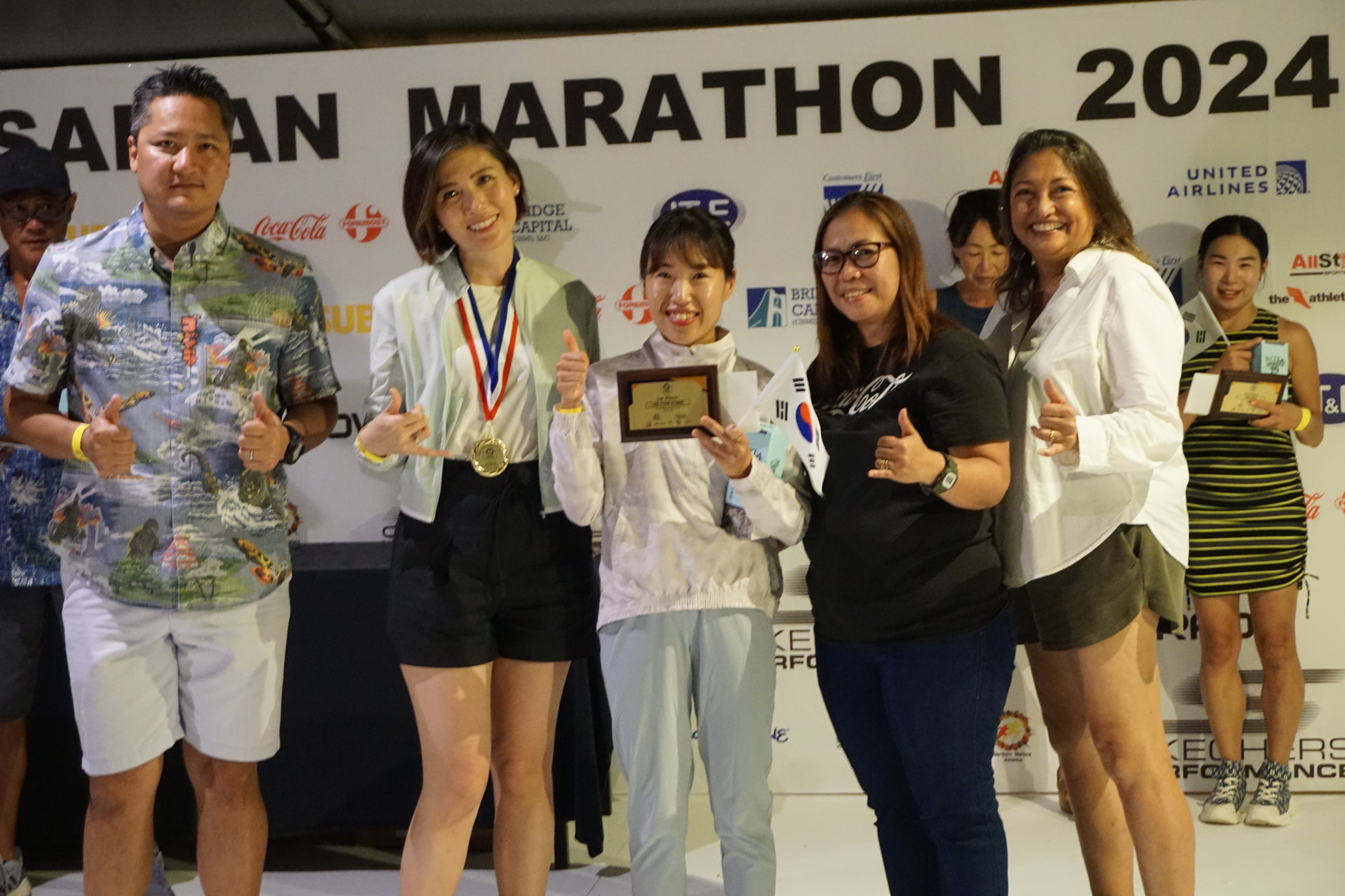Youn Kyung Lee, center, holds her 1st place plaque in the half marathon as she poses for a photo with Marianas Visitors Authority Managing Director Christopher Concepcion, Skechers representative Jennifer Tan, Coca-Cola representative Aileen Benavidez, and MVA acting Chair Gloria Cavanagh during the awards banquet at the Hyatt Regency Saipan on Saturday.